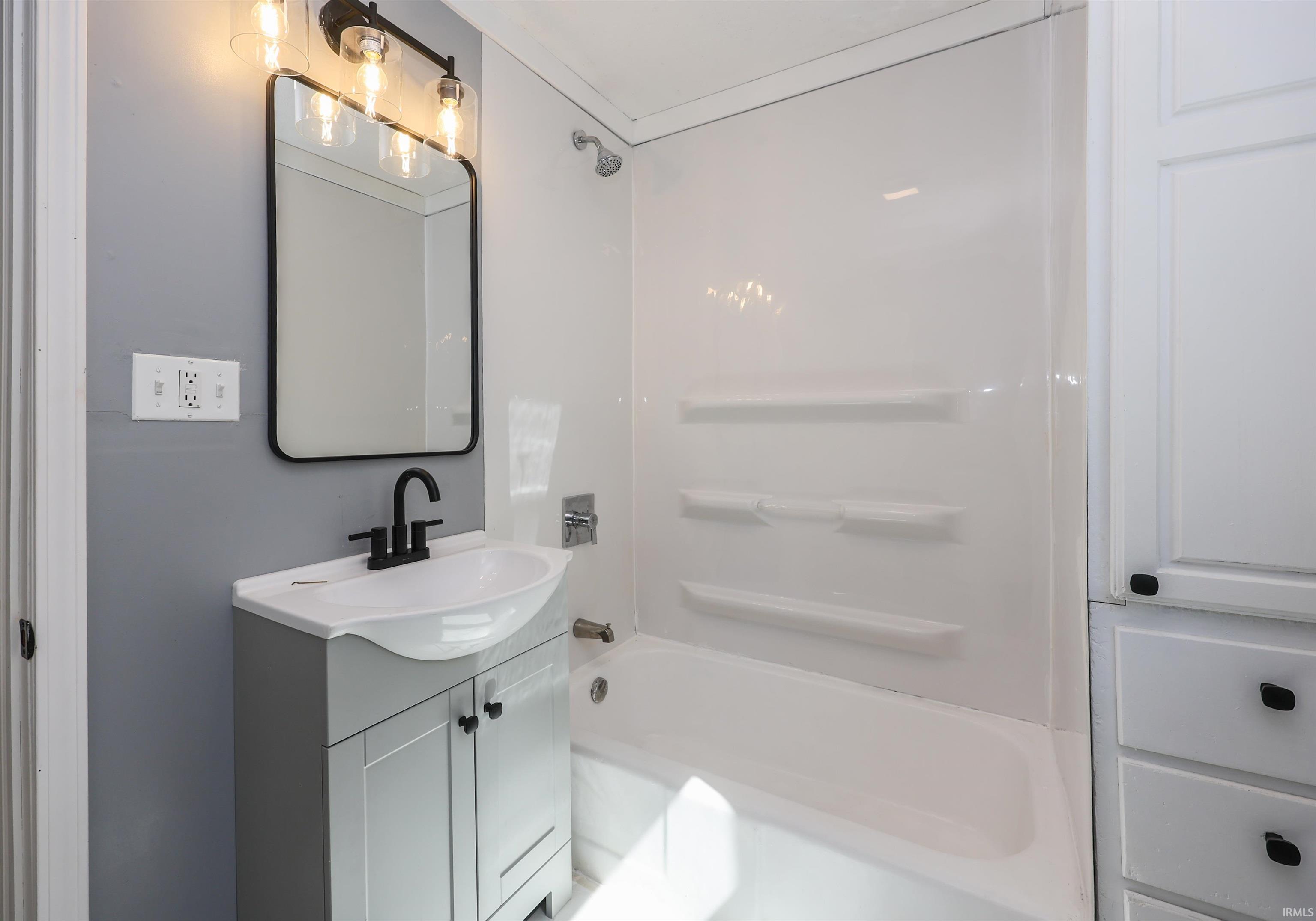 Bathroom featuring a modern vanity with integrated sink, black fixtures, rectangular framed mirror, and contemporary light fixture