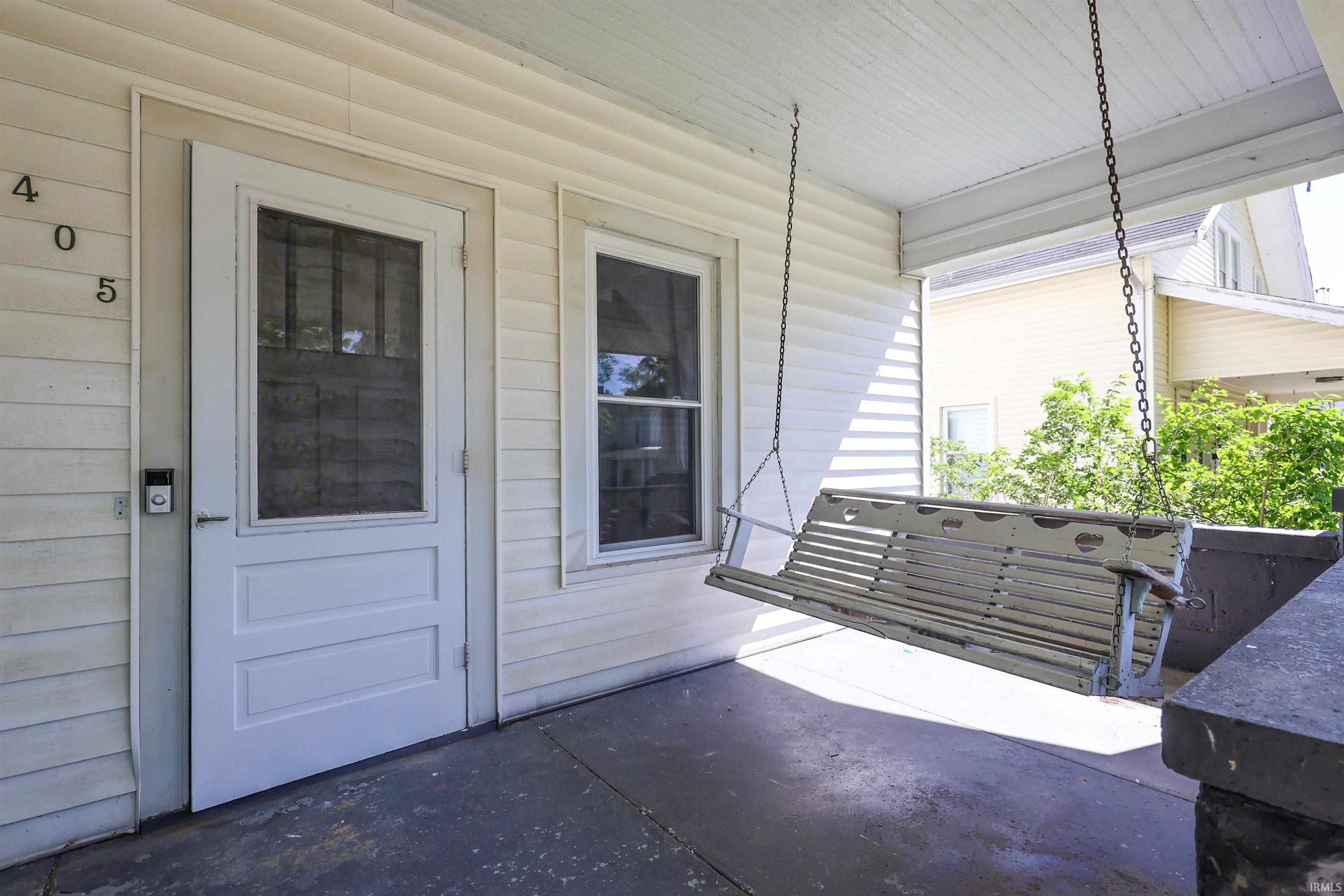 Front porch with a porch swing, white siding, and a screen door