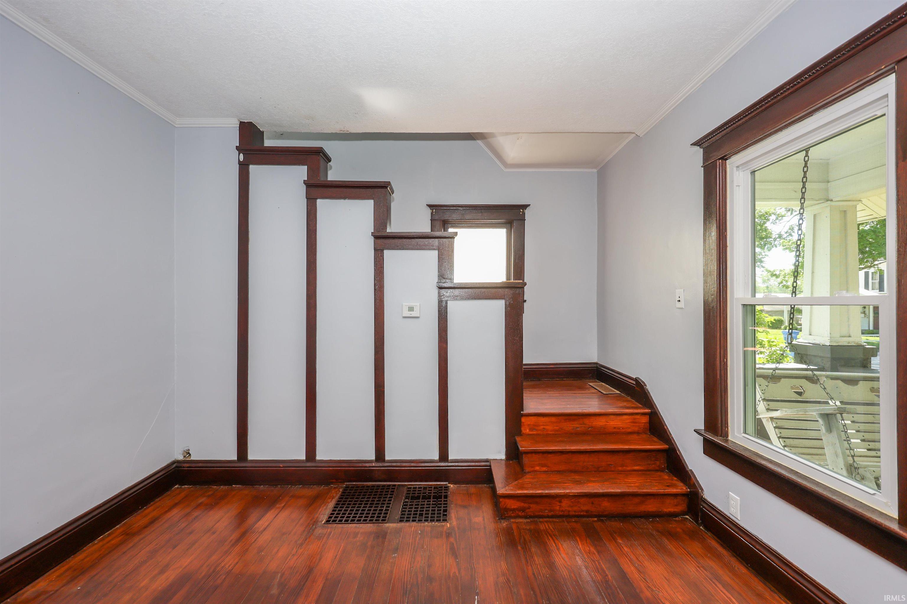 Hardwood flooring and staircase with dark wood trim, light gray walls, and white ceiling crown molding