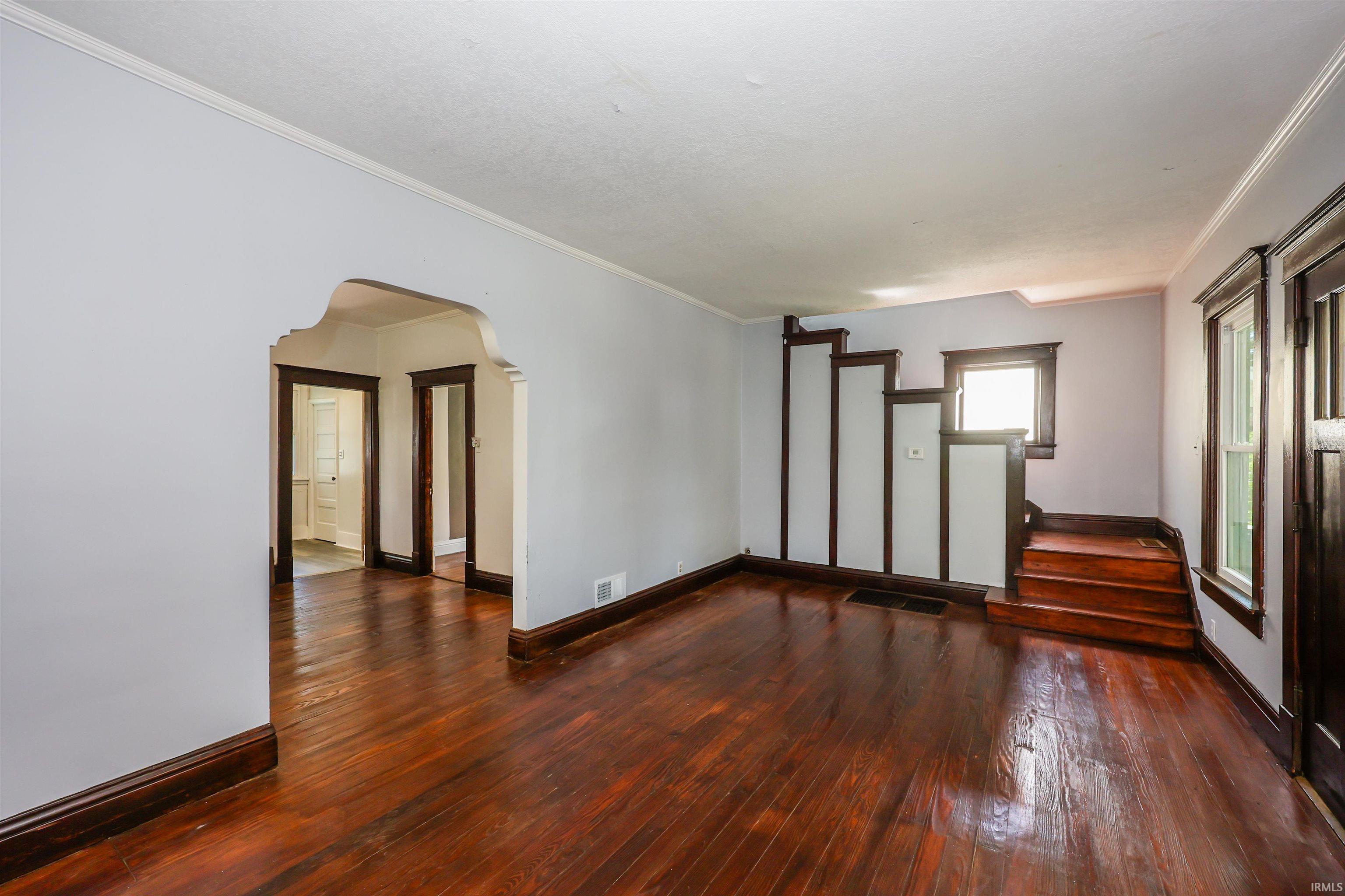 Hardwood flooring extends throughout this room, featuring an arched doorway and dark wood trim