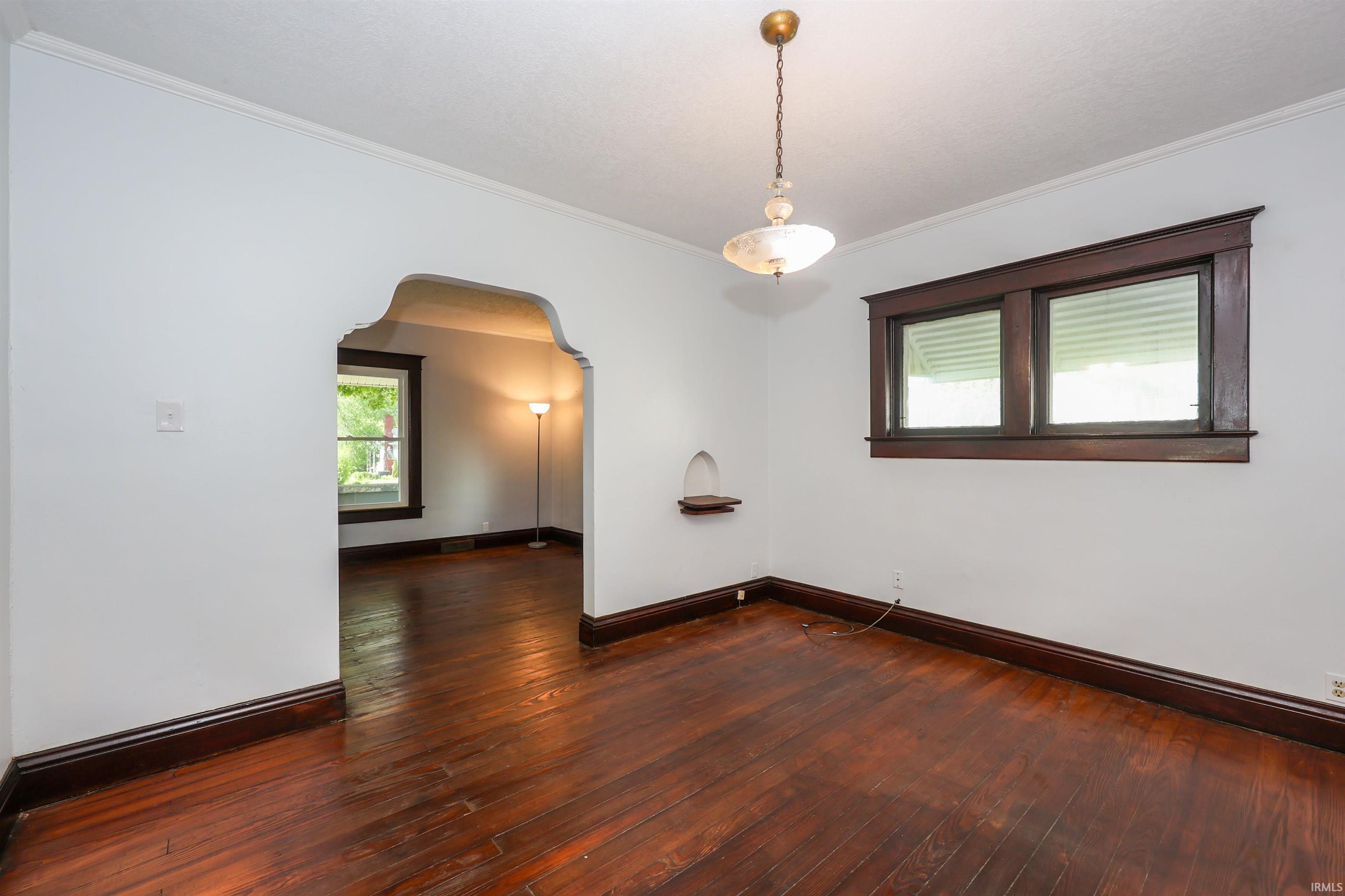 Hardwood flooring, decorative arched entryway, dark wood trim, built-in wall niche, and an overhead light fixture