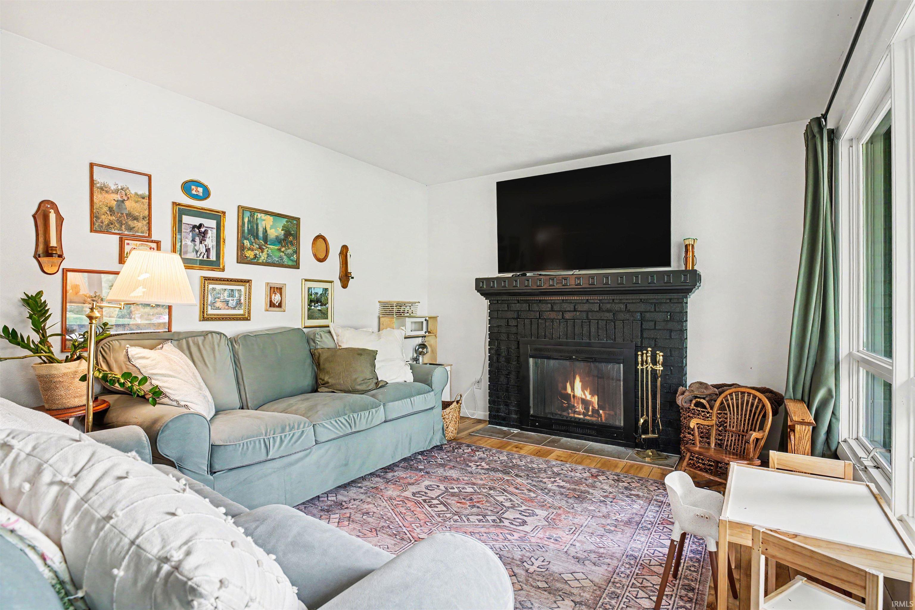 Living room featuring a black brick fireplace with a hearth, wood-finish flooring, and white walls