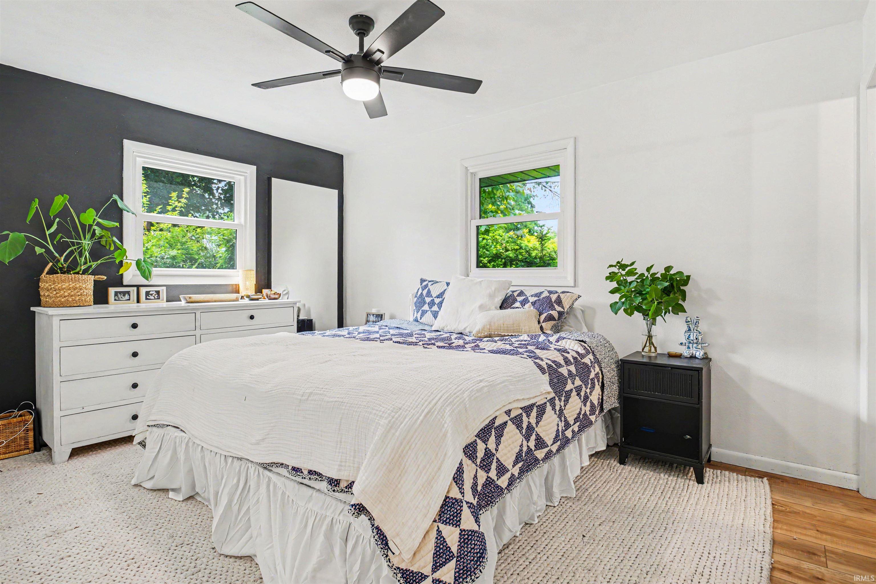 Bright room featuring white walls, a dark accent wall, two windows, and a ceiling fan with integrated lighting