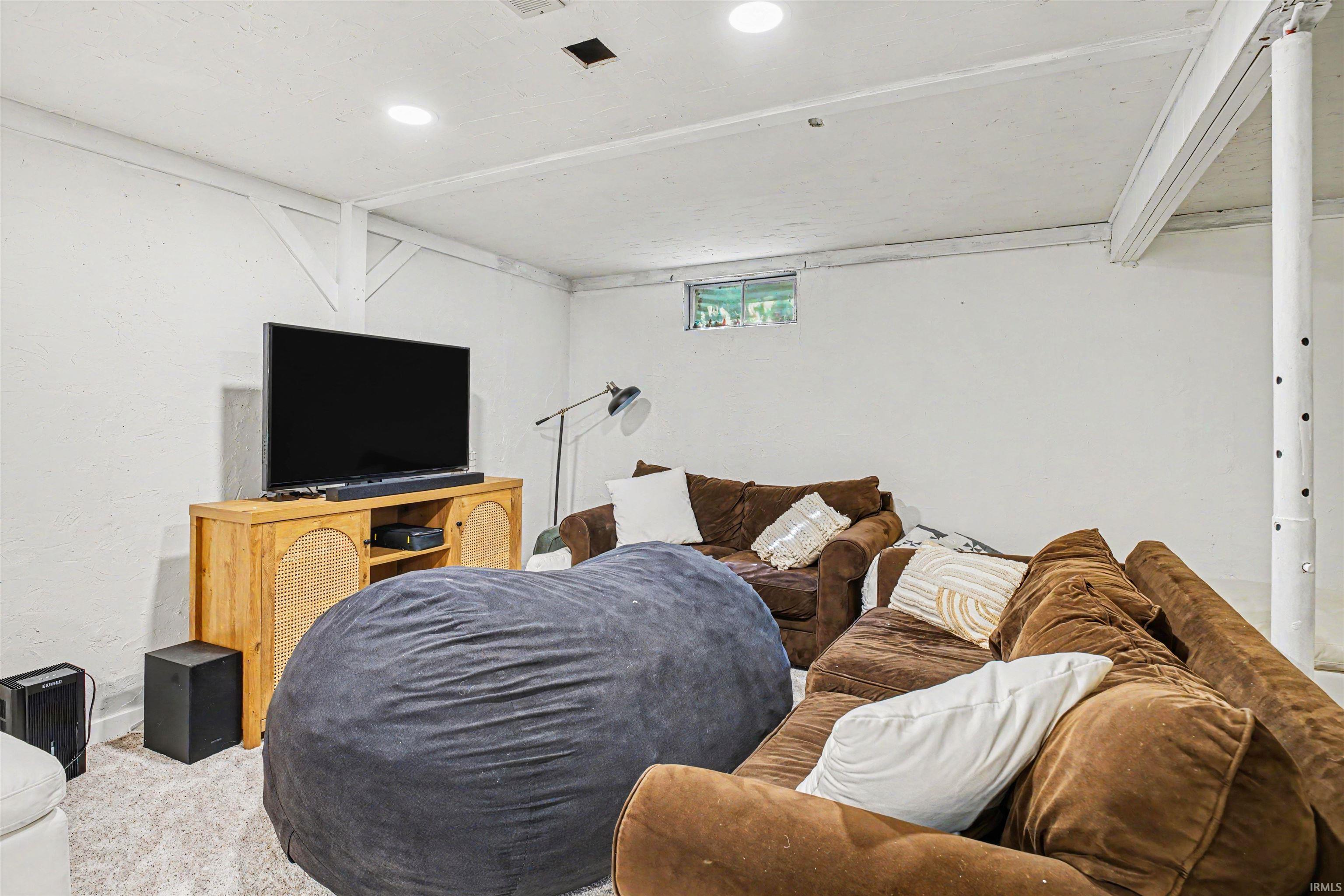 Recessed lighting illuminates this versatile space featuring white-painted exposed ceiling joists and support beams