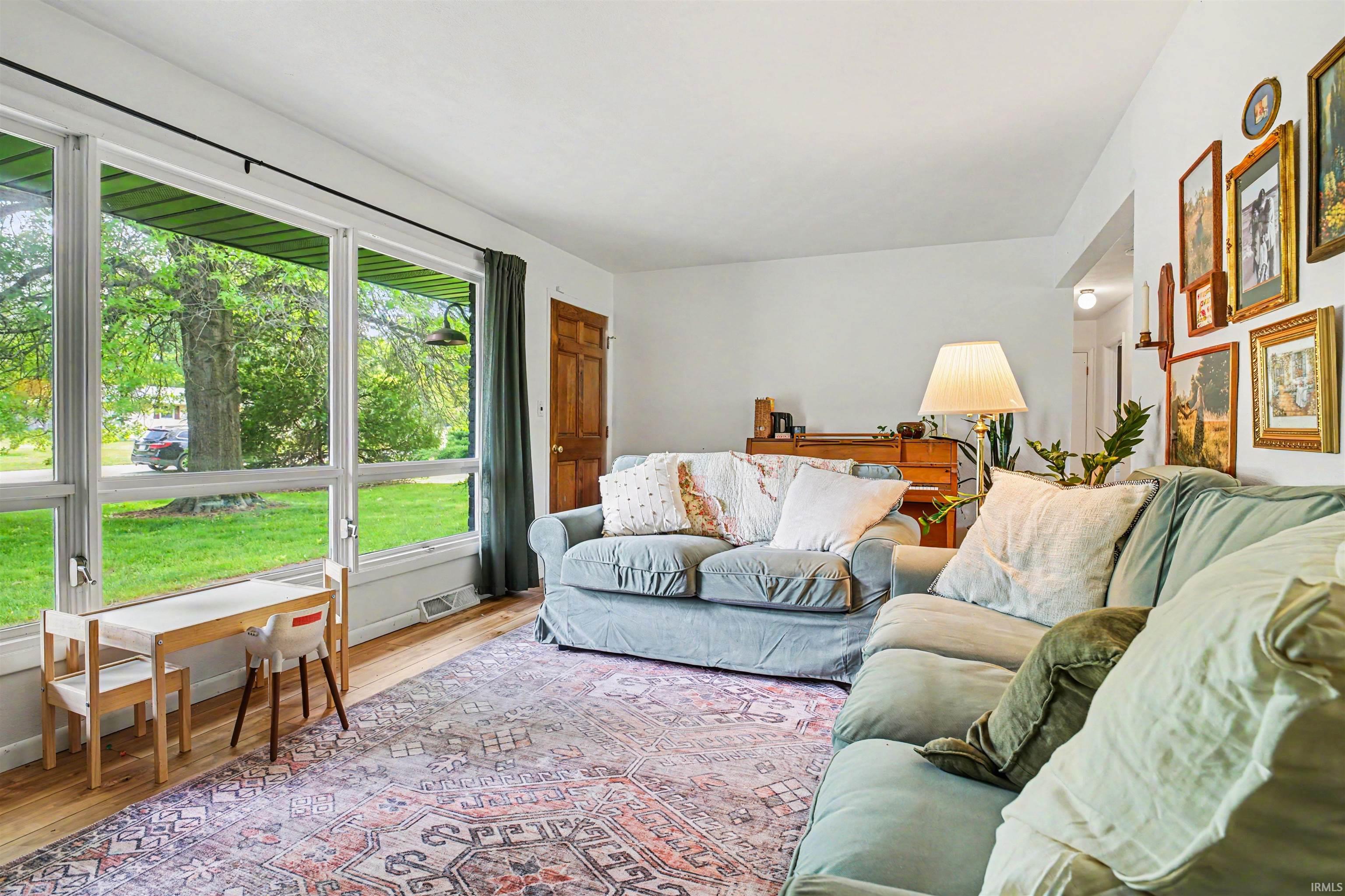 Bright living space featuring expansive windows, wood-finish flooring, a paneled wood entry door, and a white wall finish