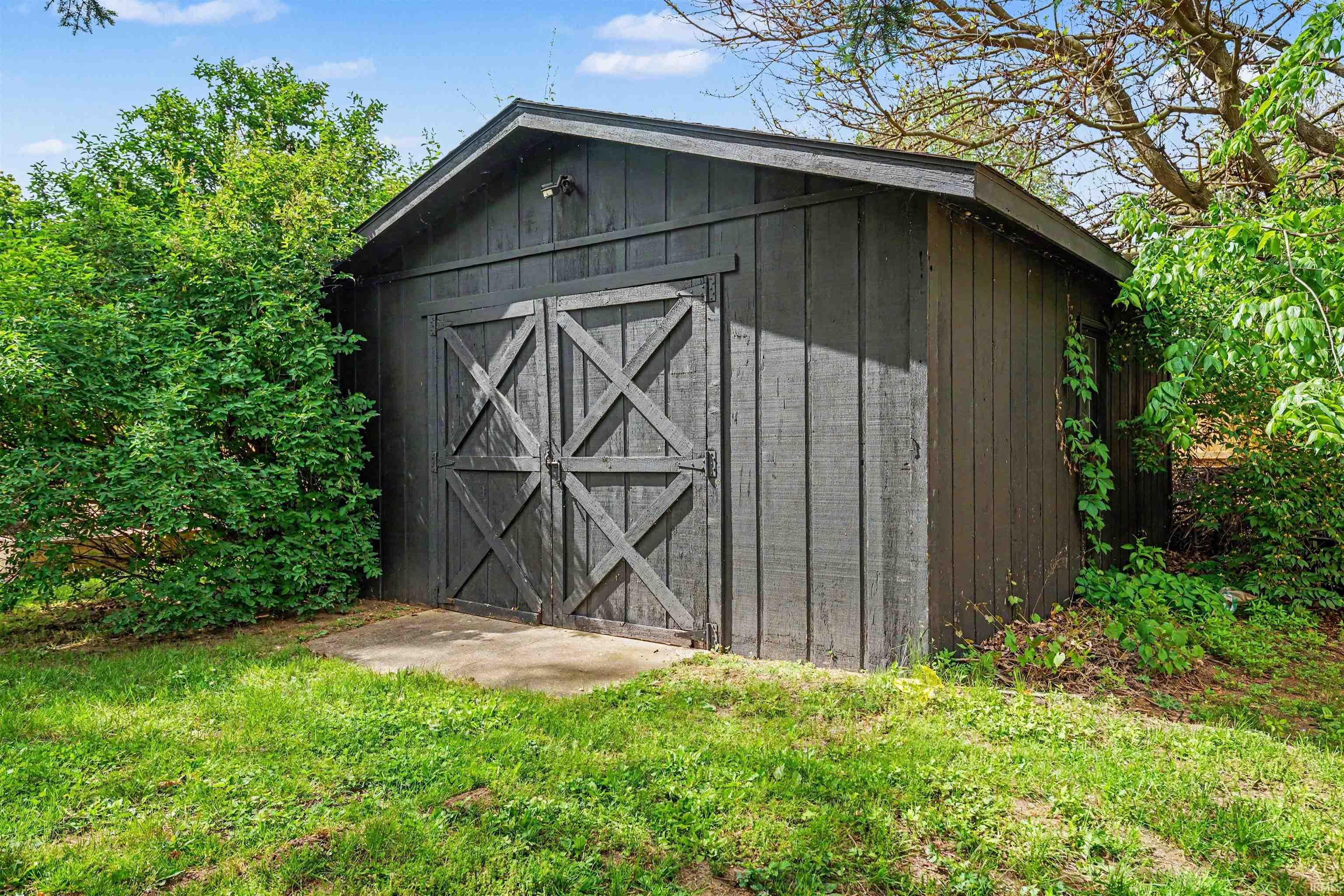 Freestanding storage shed featuring dark-stained vertical plank siding and a pitched roof