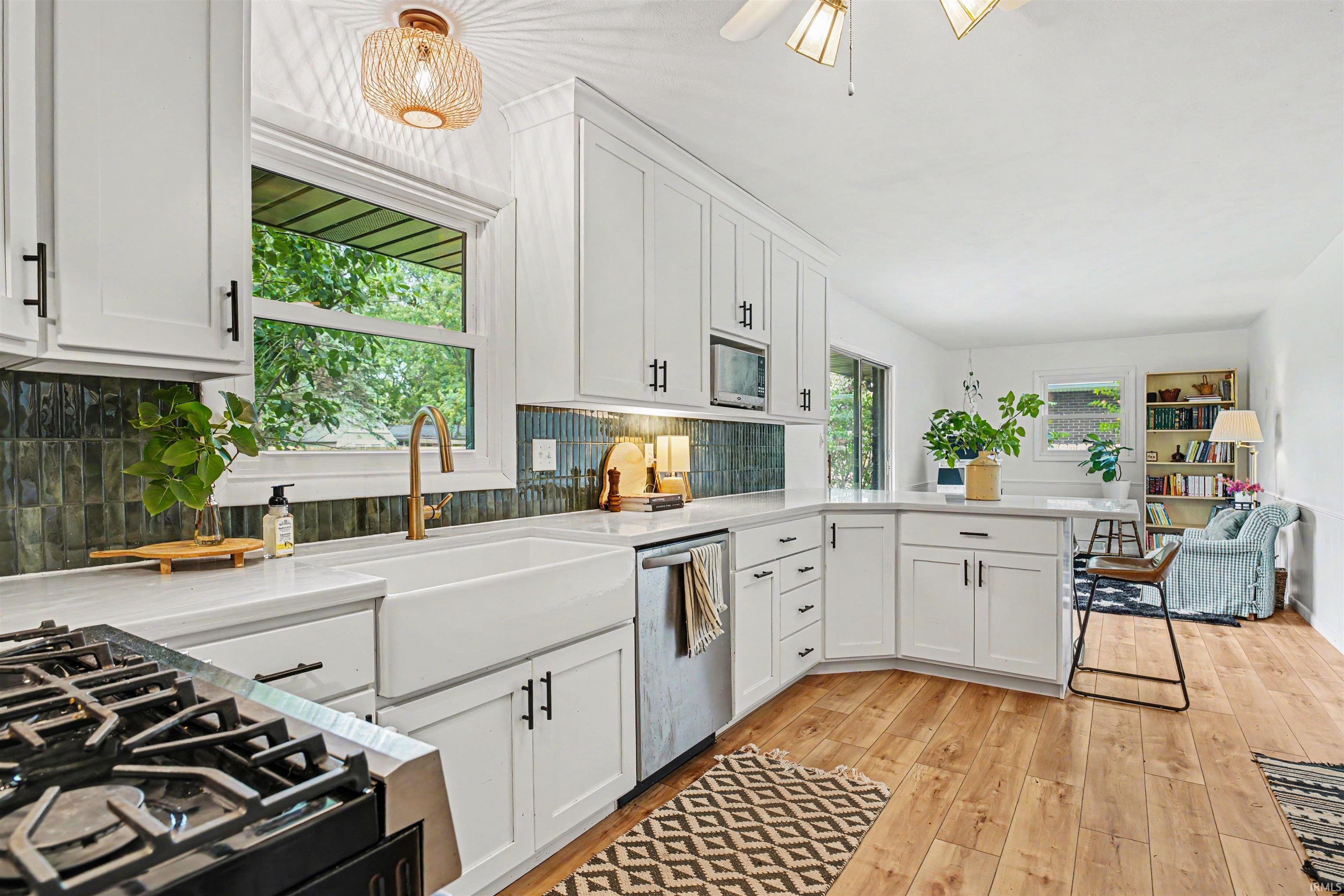 Kitchen featuring white shaker cabinetry with black hardware, a farmhouse-style sink, white countertops, and a dark tile backsplash