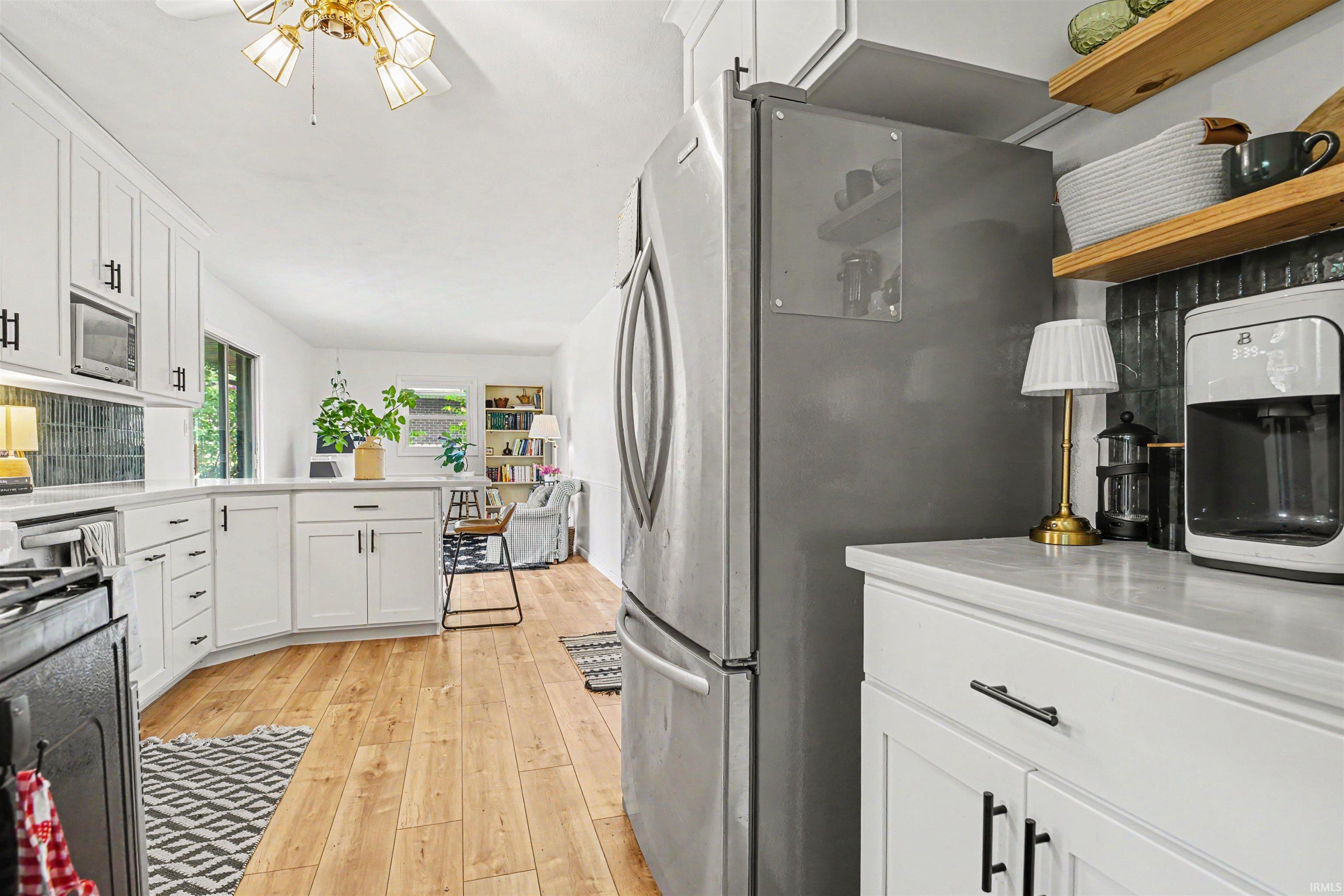 Modern kitchen featuring white cabinetry, light wood-finish flooring, a dark tile backsplash, and stainless steel appliances