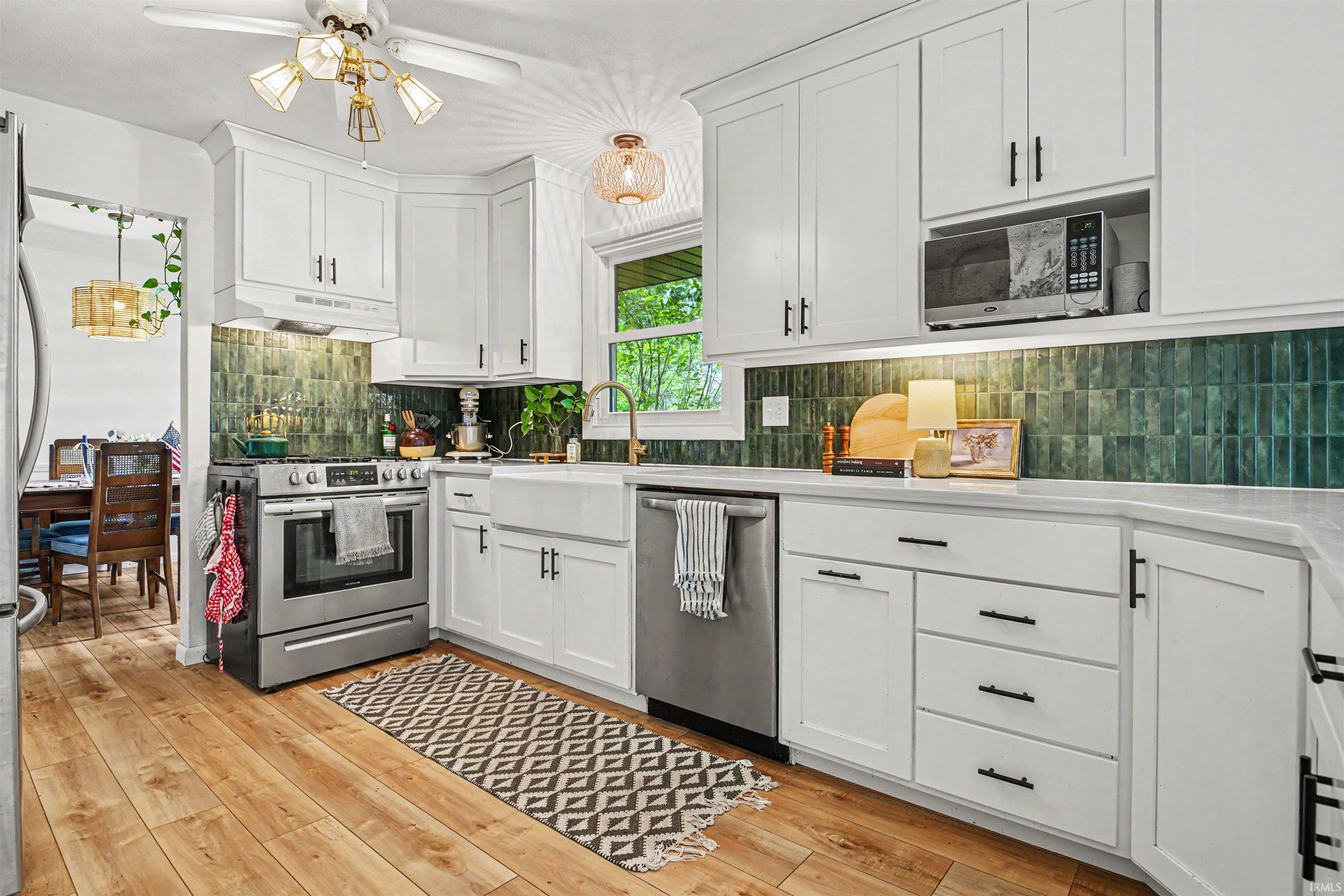 Bright kitchen featuring white cabinetry, stone-finish countertops, stainless steel appliances, and wood-finish flooring