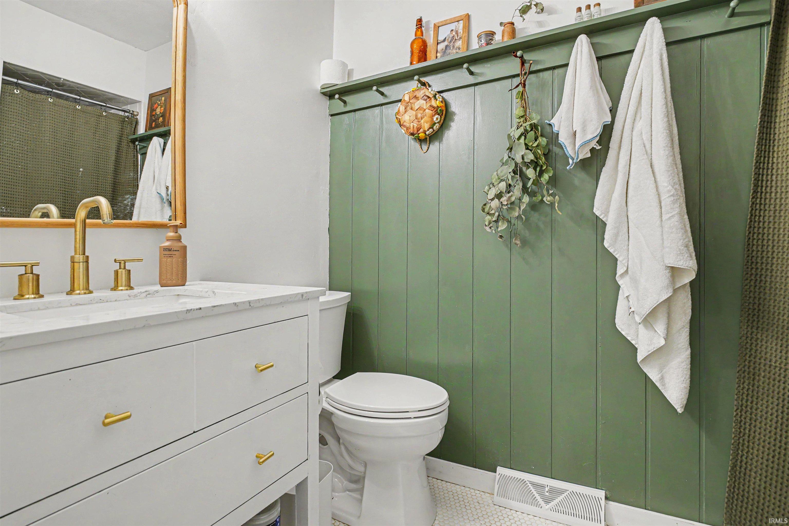 Bathroom featuring a white vanity with gold-tone hardware, a white countertop, and a gold-framed mirror