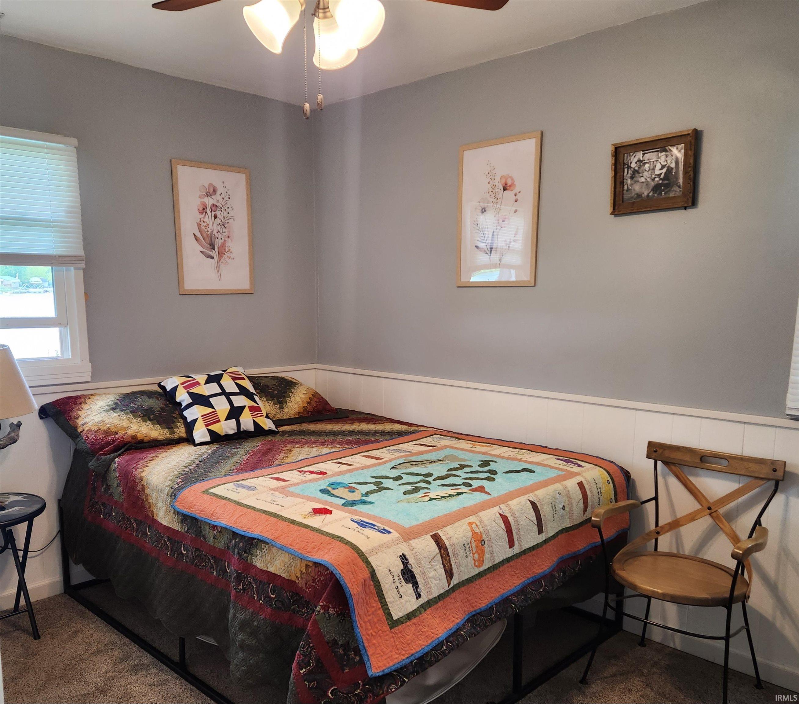 Recessed window with horizontal blinds, overhead ceiling fan with light fixture, gray wall paint, and white wainscoting