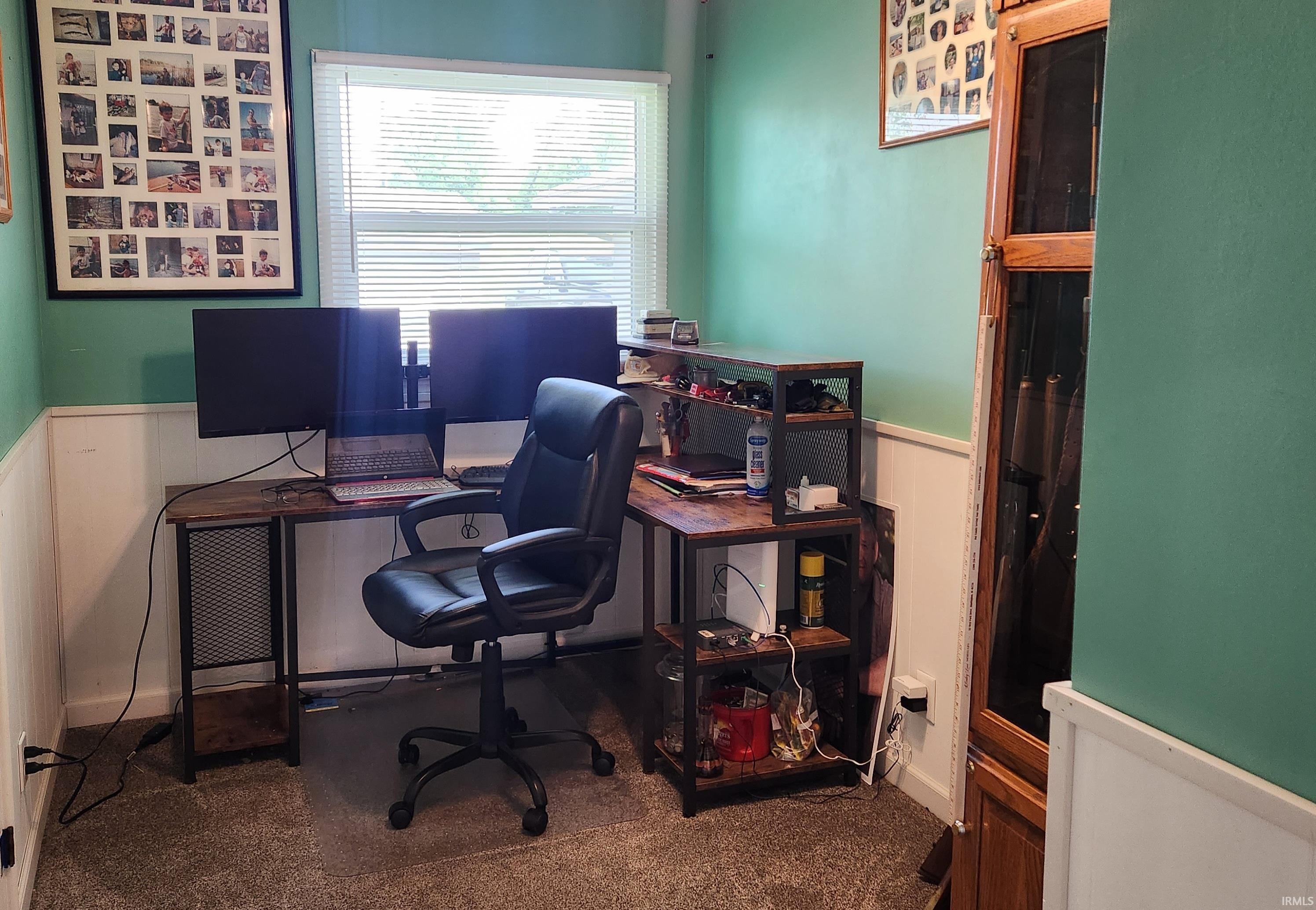 Carpeted room featuring a window with blinds, two-tone wall treatment with wainscoting, and a built-in wooden display cabinet