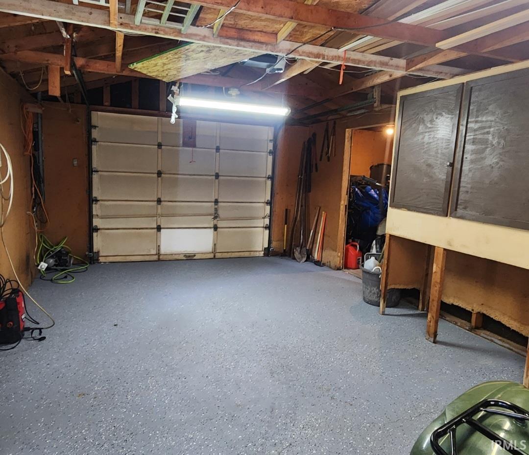 Garage space featuring a roll-up door, exposed ceiling joists, and a speckled gray floor finish