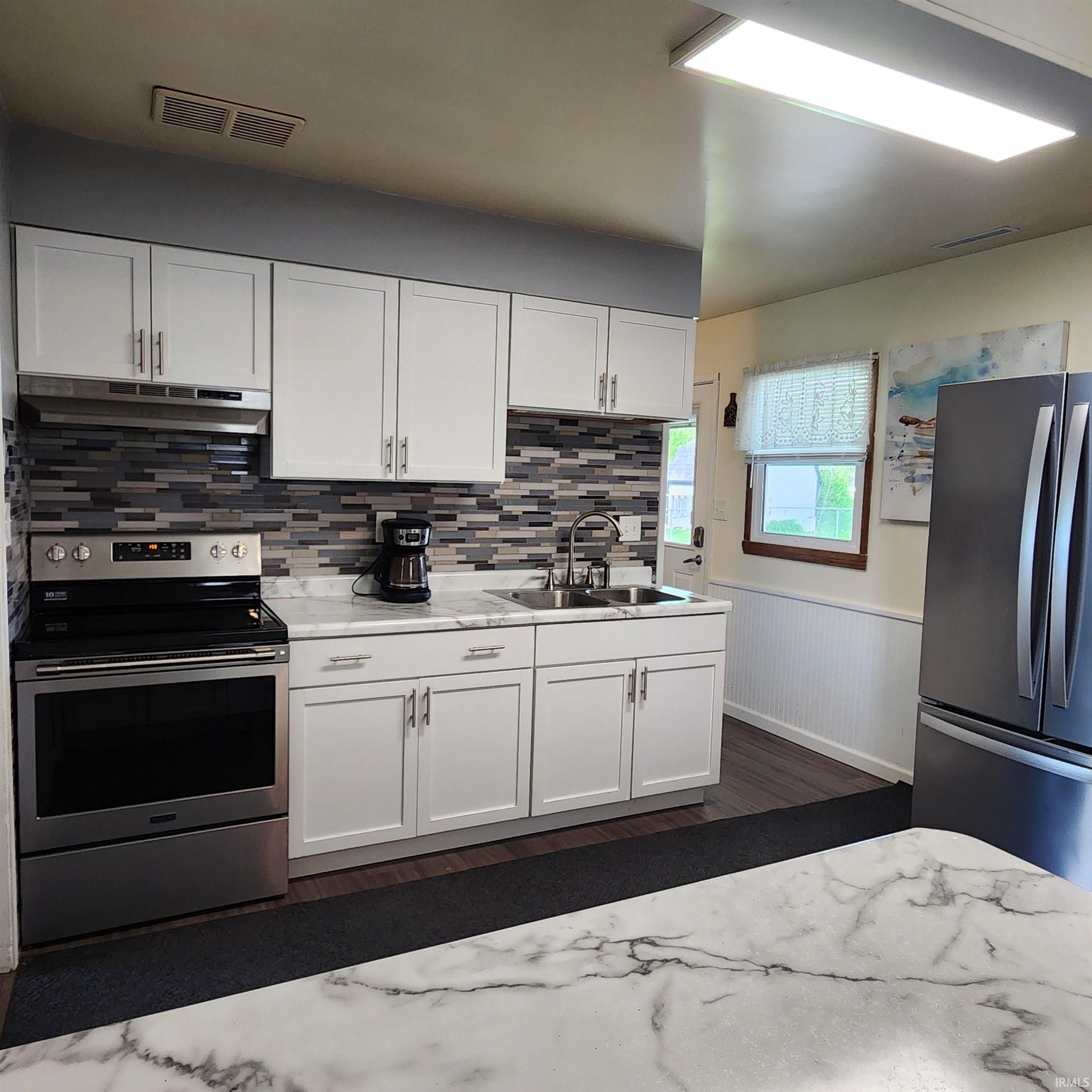 Kitchen featuring white cabinetry, a mosaic tile backsplash, stainless steel appliances, and stone-finish countertops