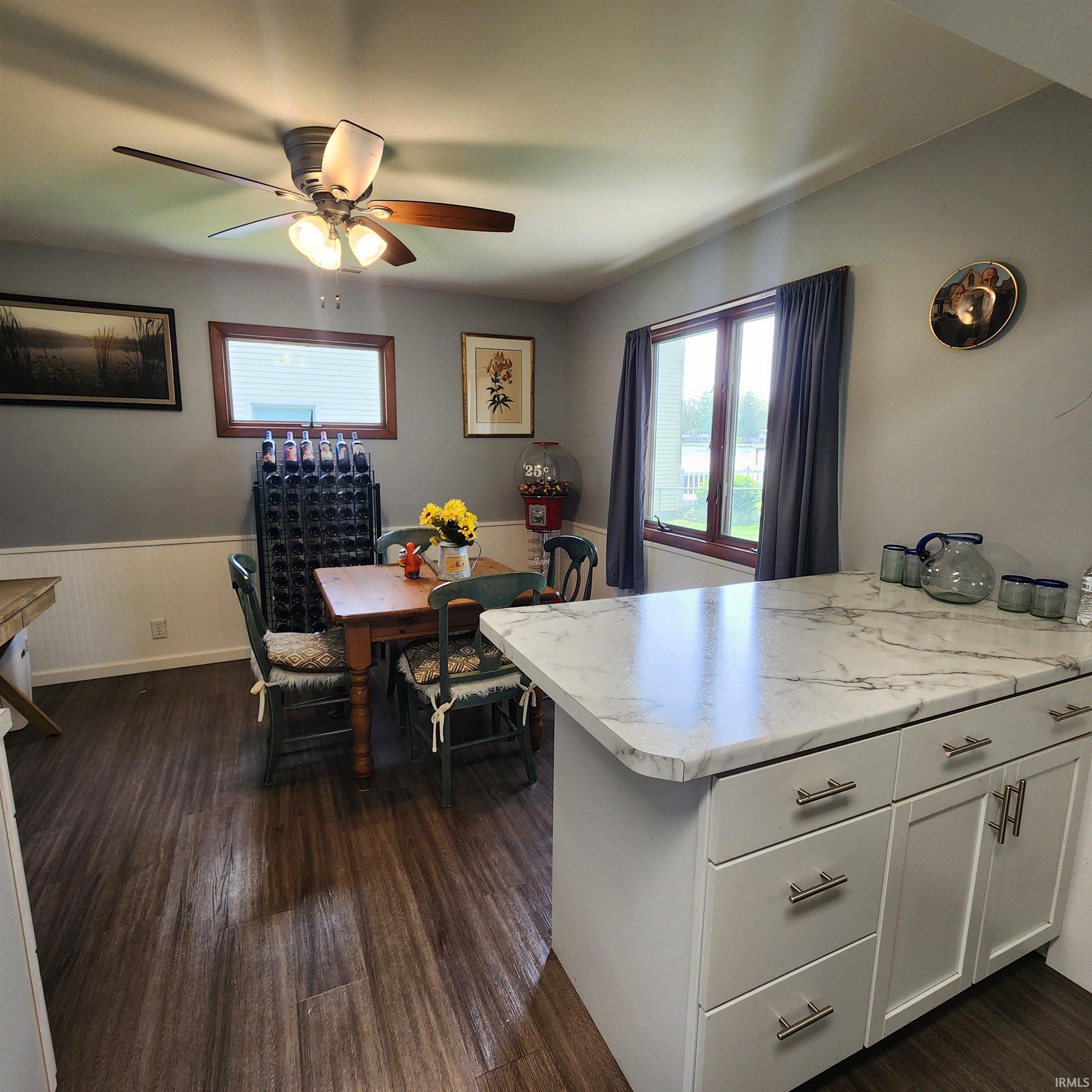 Kitchen area featuring wood-finish flooring, a ceiling fan with light fixture, and a window with wood trim