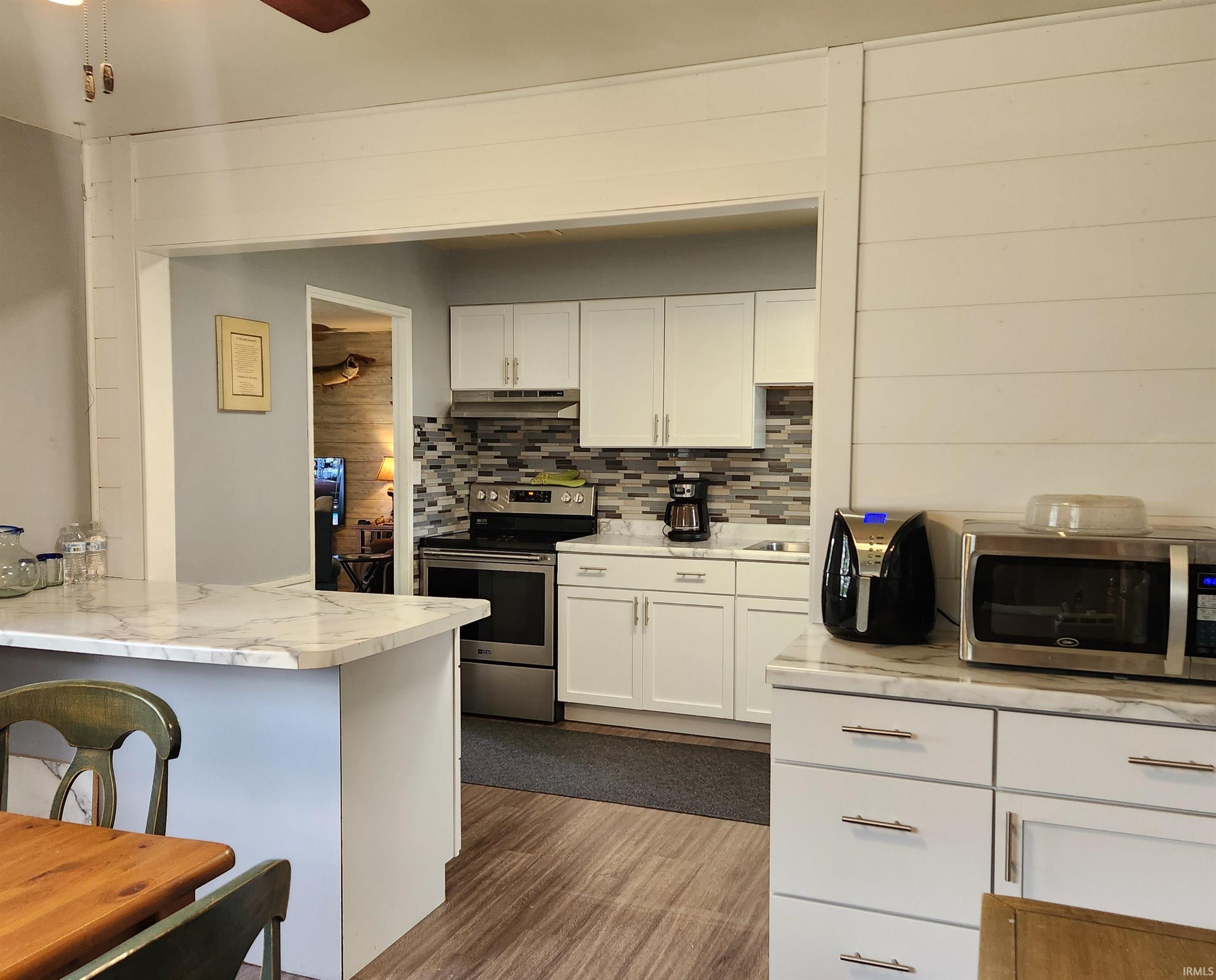Kitchen featuring white shaker-style cabinetry, stainless steel appliances, wood-finish flooring, and a marble-finish countertop island