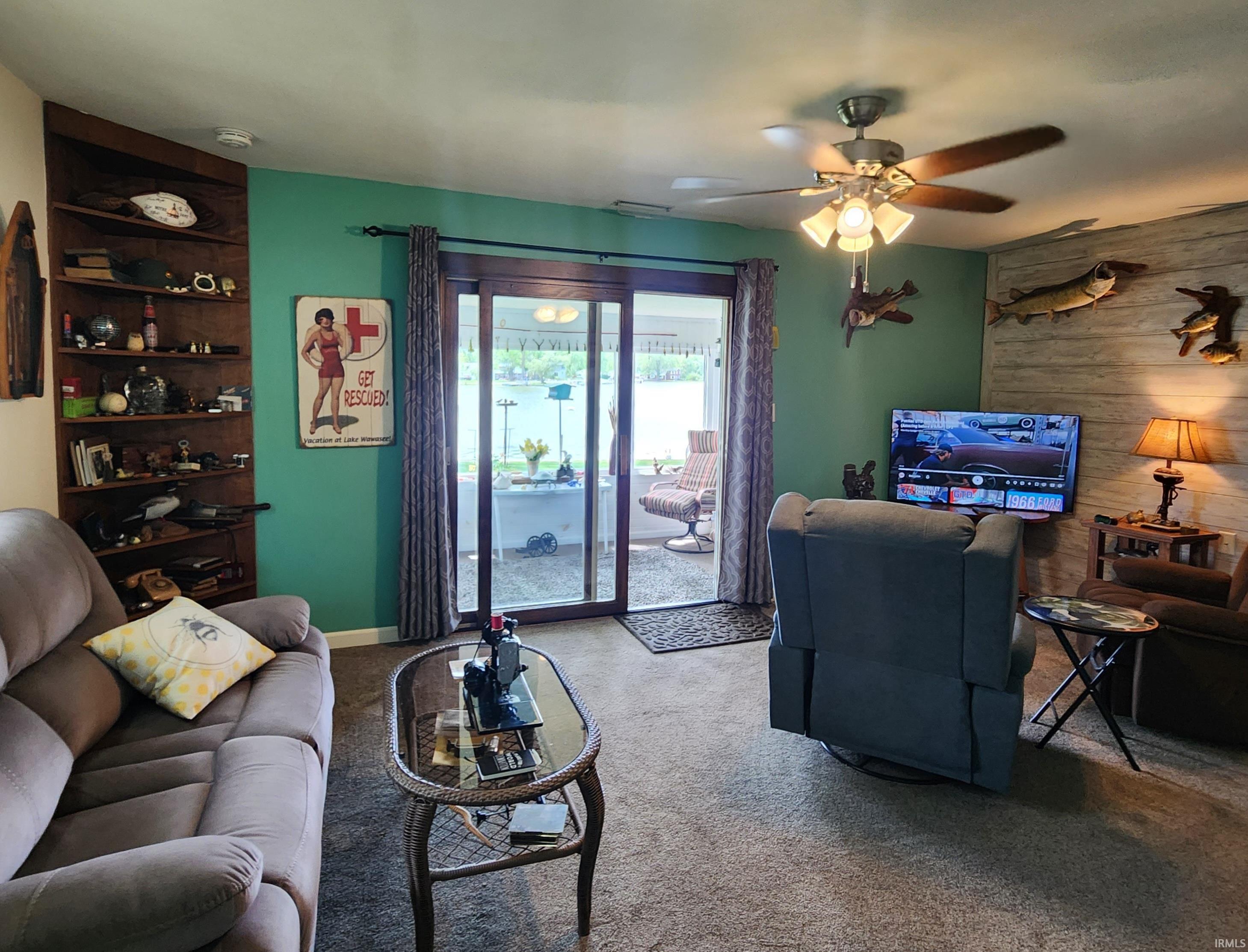 Living area featuring sliding glass doors to the outdoor space, a built-in corner shelving unit, a ceiling fan with integrated lighting, and a textured accent wall