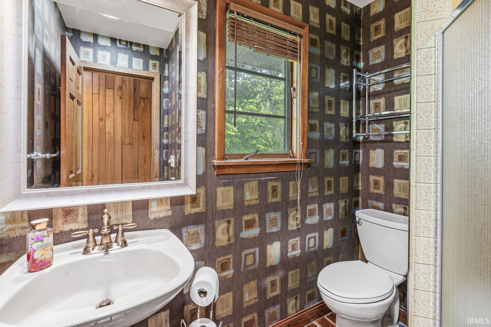 Pedestal sink with brass-finish faucet, framed mirror, and window with natural wood trim