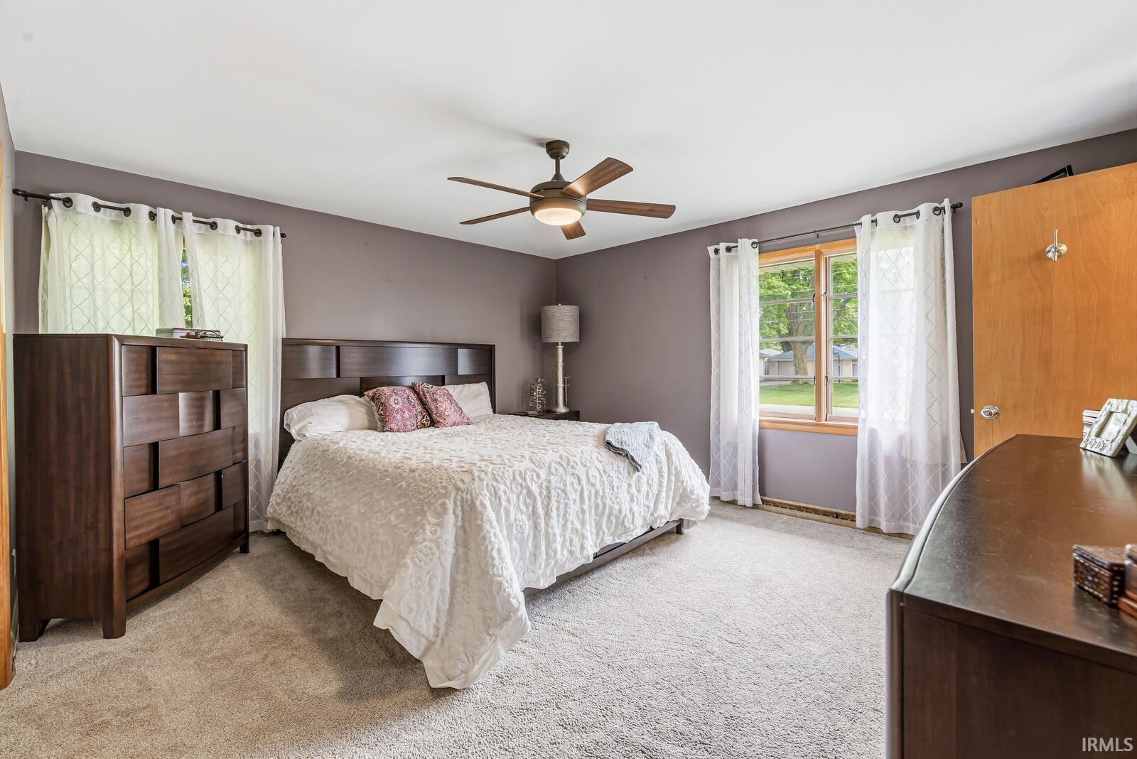 Carpeted room featuring a ceiling fan with integrated lighting, wood-trim windows, and a solid wood door