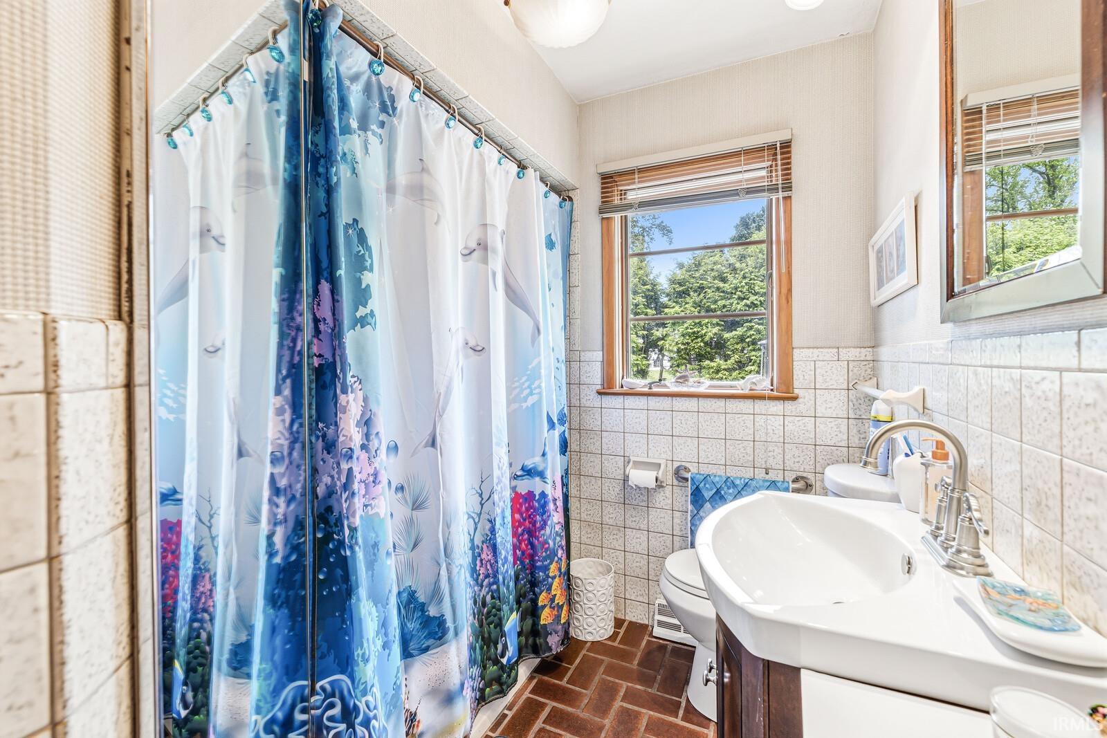 Bathroom featuring a wood-frame window, white square wall tiling, and rich brown herringbone-patterned floor tiles
