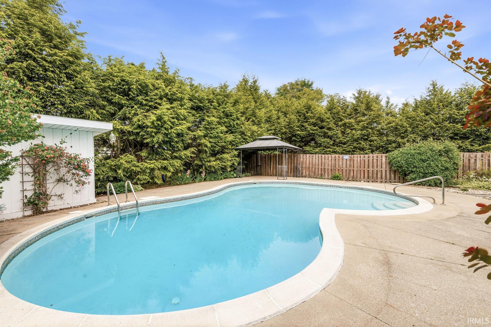 Freeform inground pool featuring integrated steps and a surrounding concrete patio
