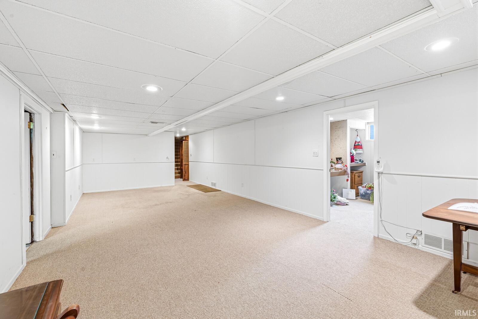 Finished basement space with recessed lighting, light-toned carpeting, white paneling, and drop ceiling