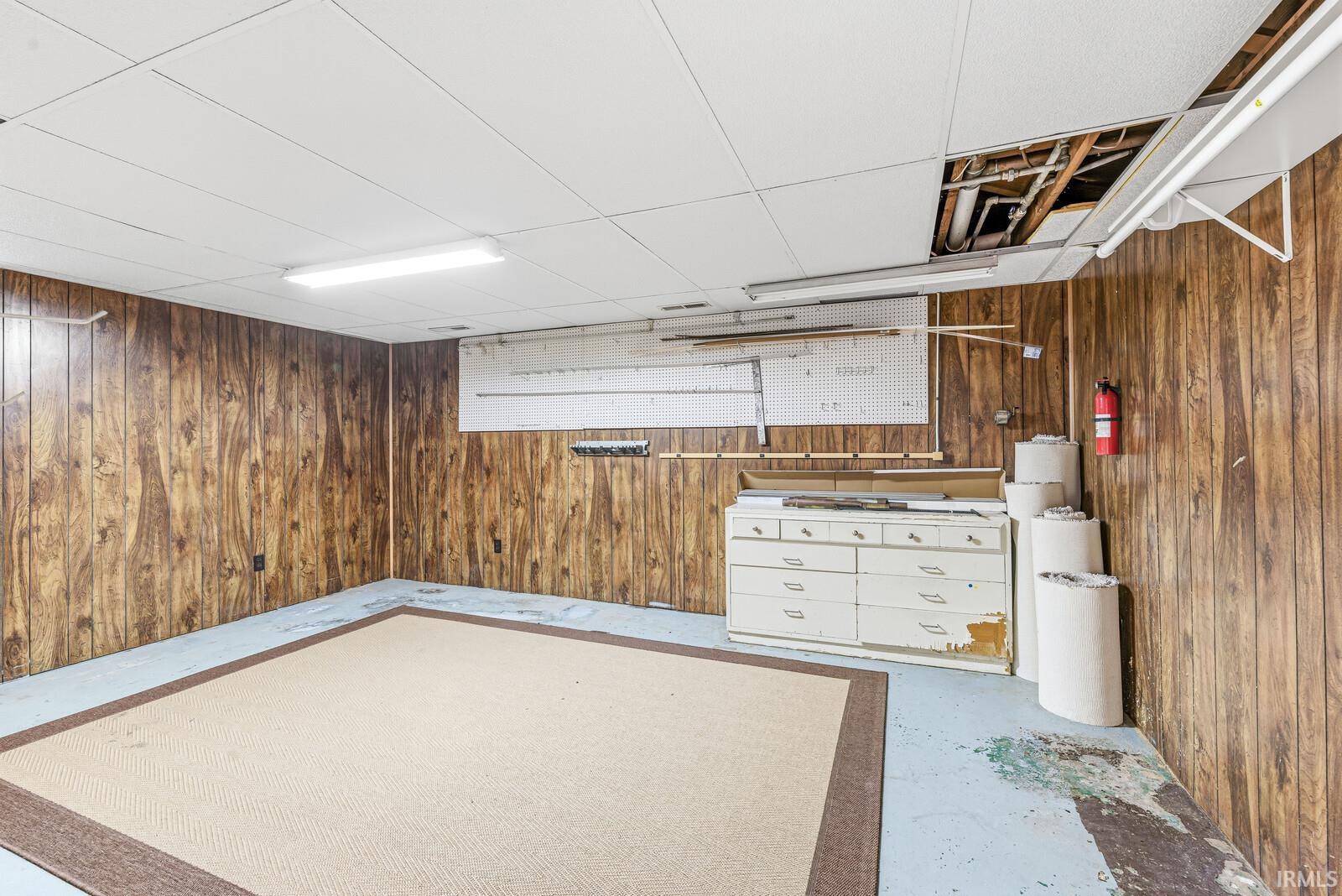 Basement room featuring wood paneling, drop ceiling, and concrete flooring