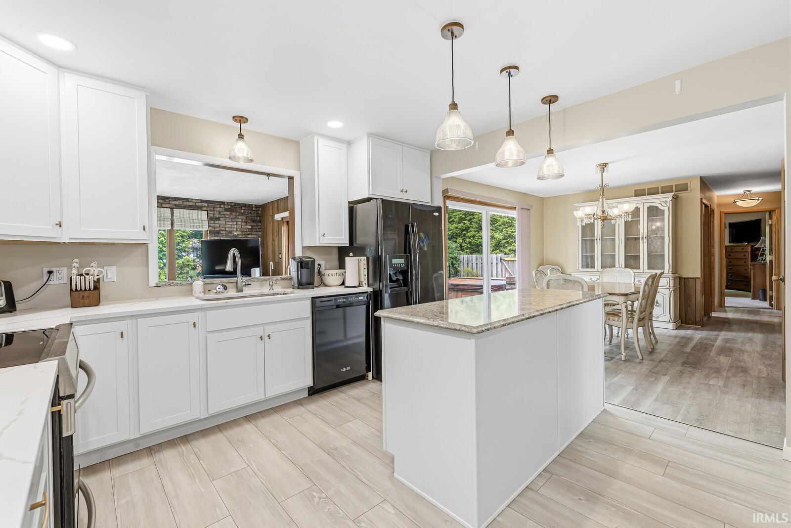 Kitchen featuring white cabinetry, light-toned wood-finish flooring, a central island with a stone countertop, a black appliance suite, and recessed lighting