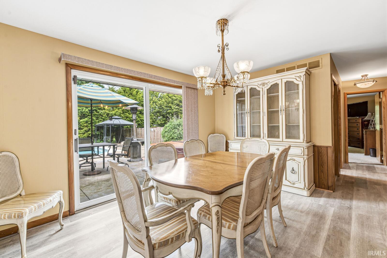 Sliding glass door opening to a paved patio, light-toned wood-finish flooring, and an ornate chandelier