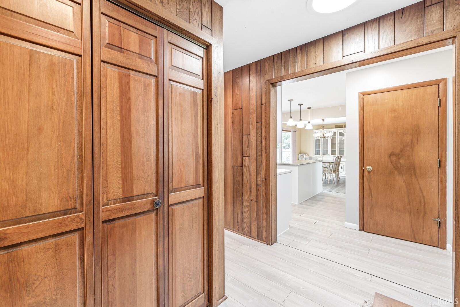 Wood-paneled hallway featuring light wood-finish doors, a flush-mount ceiling light, and light-toned tile flooring