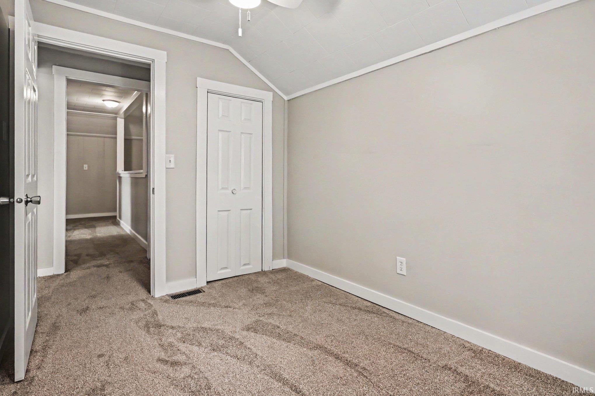 Carpeted room featuring a white bi-fold closet door, neutral wall color, white trim, and an angled ceiling