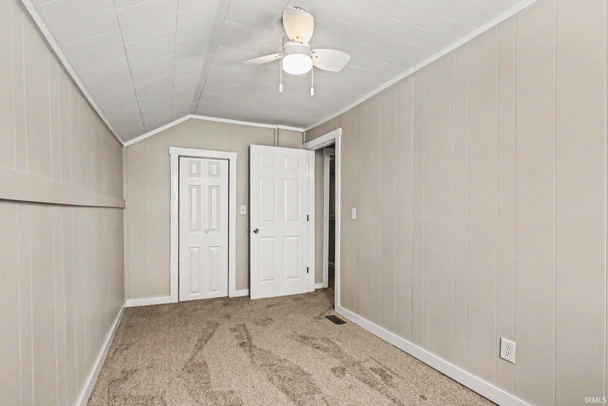 Carpeted room featuring vertical paneling, two white paneled doors, and a ceiling fan with integrated lighting