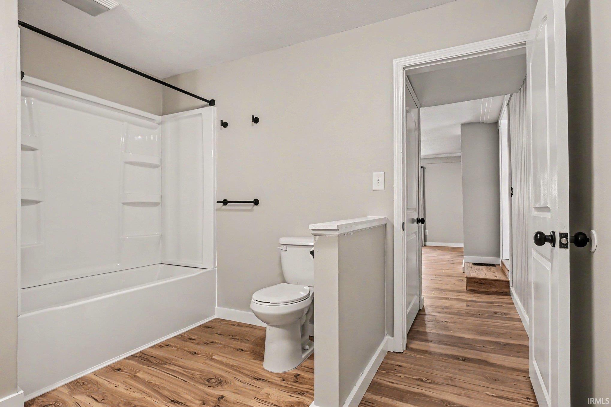 Bathroom featuring a white tub-shower combination with built-in shelving, wood-finish flooring, and light neutral wall paint