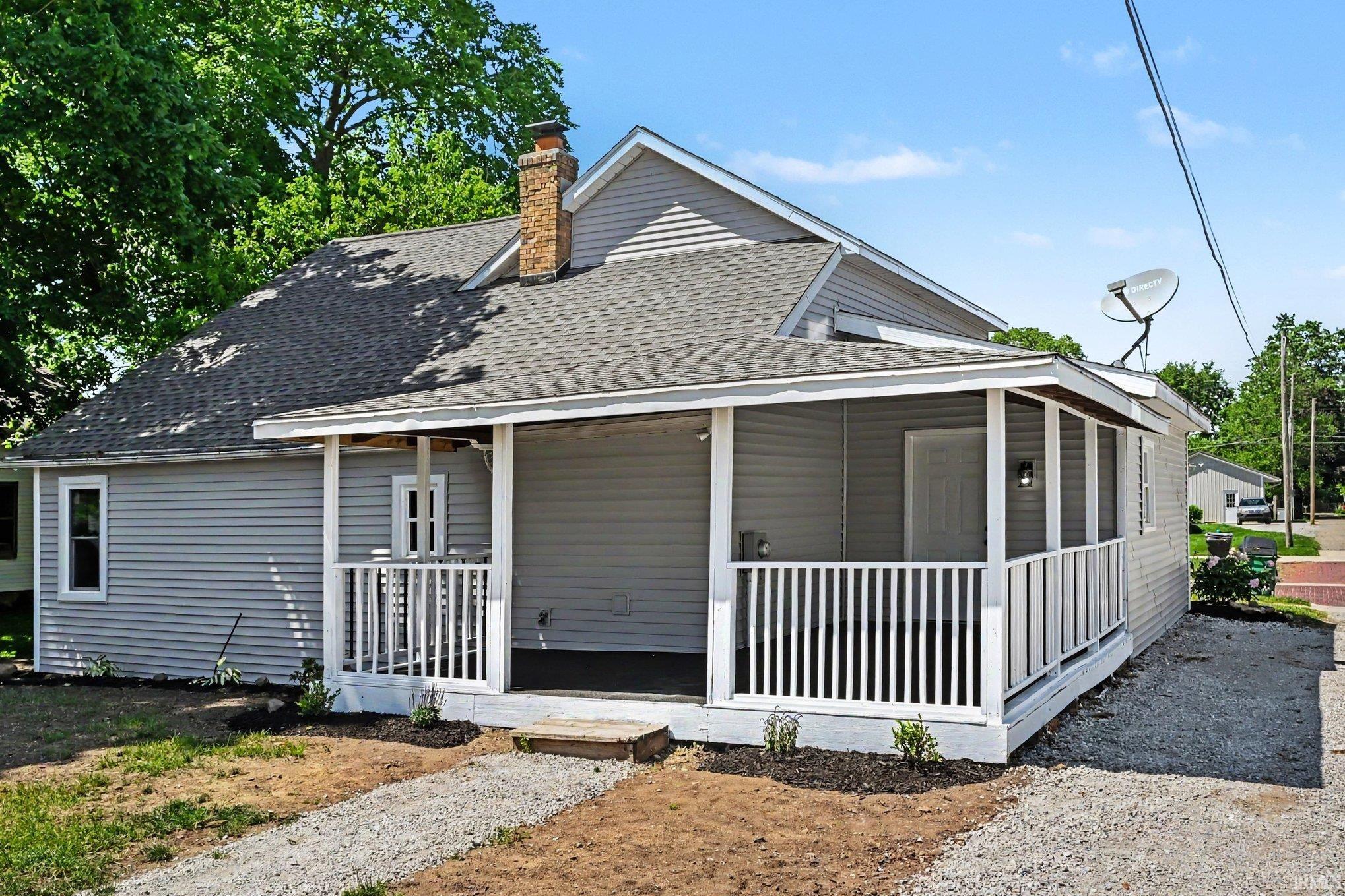 Exterior featuring a wrap-around porch with white railings, light gray siding, and a gabled roof