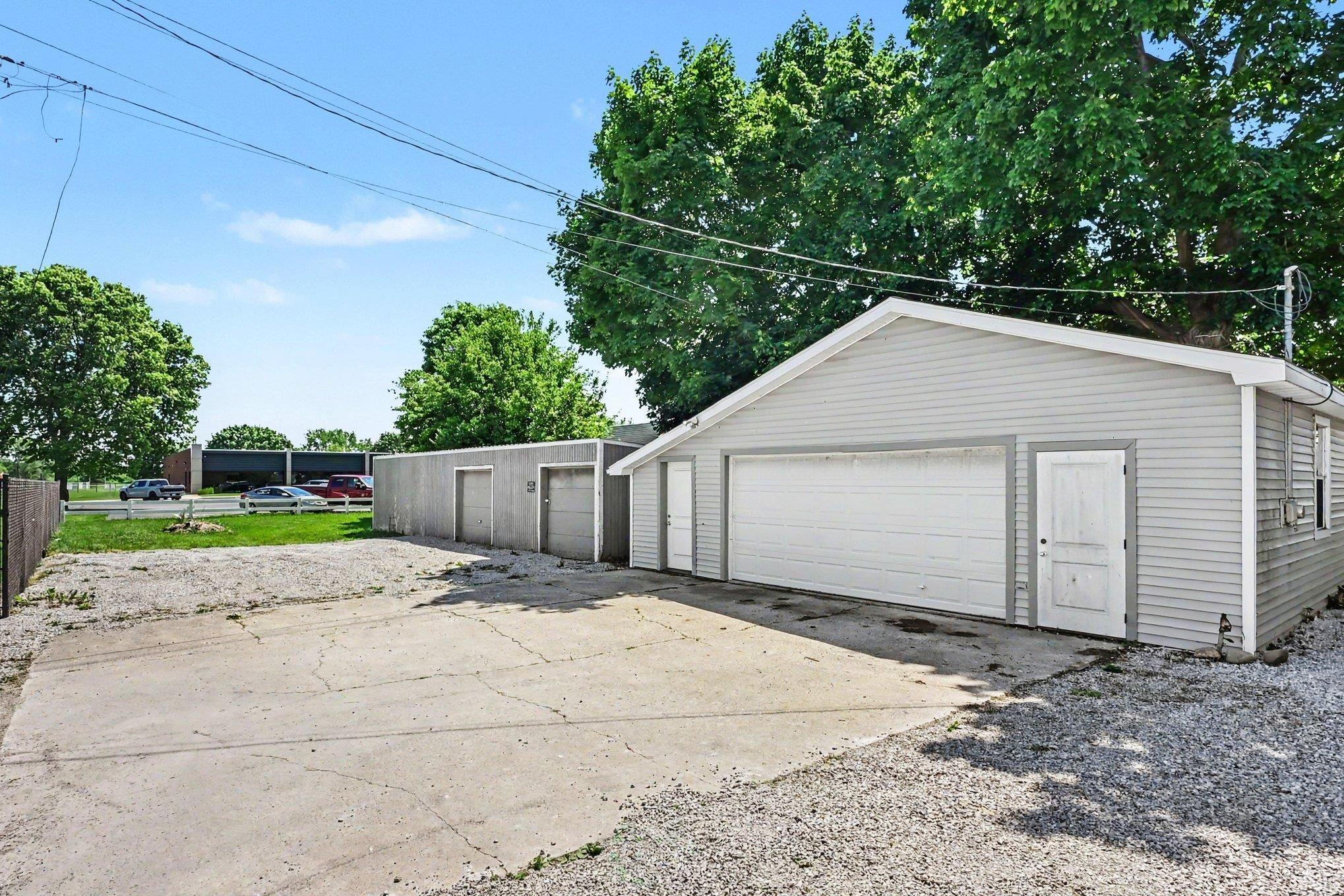 Detached gray garage structure featuring a main overhead door, side entry door, and vinyl siding