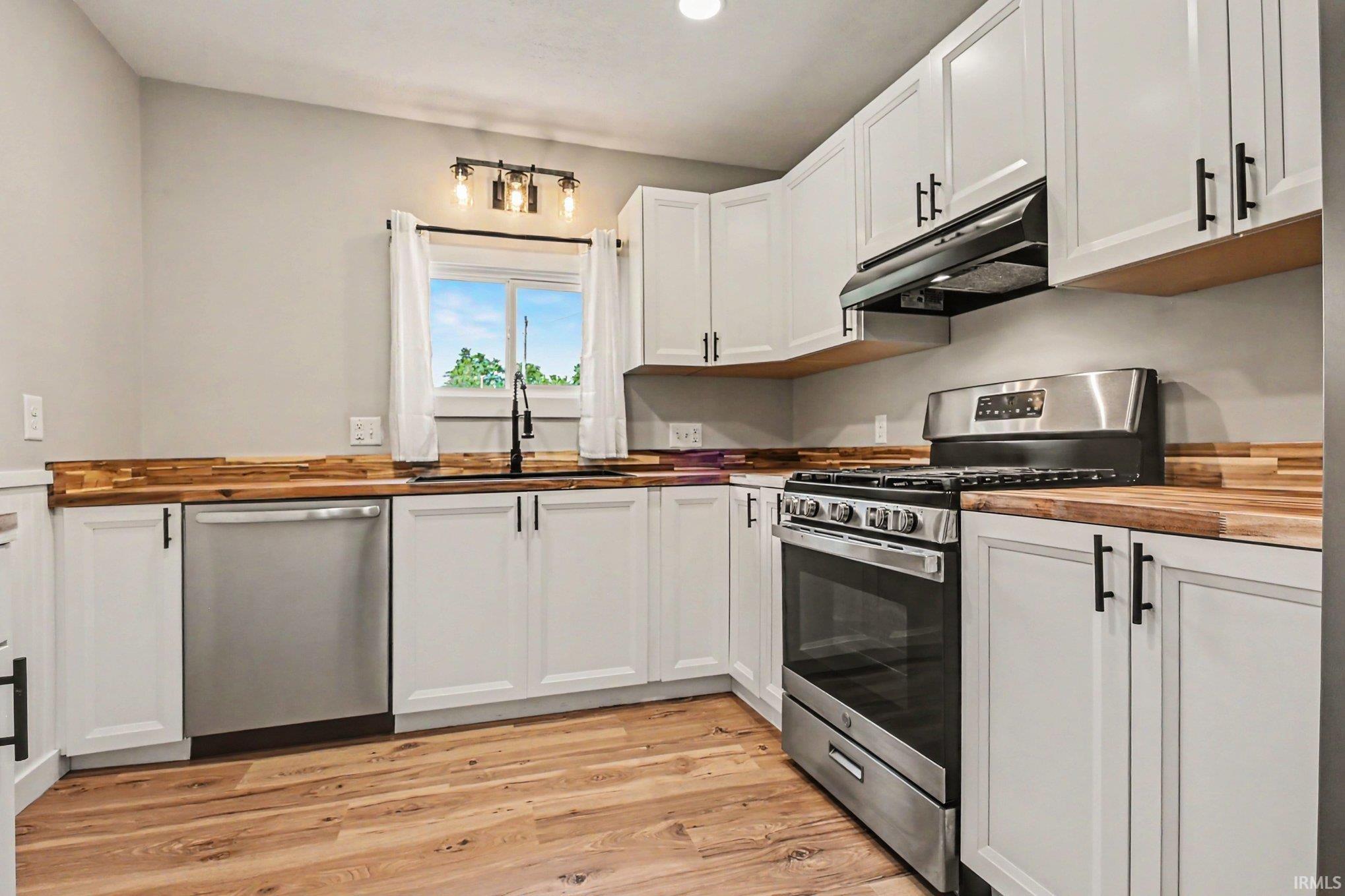 Modern kitchen featuring white cabinetry with black hardware, wood-finish countertops, stainless steel appliances, and wood-finish flooring