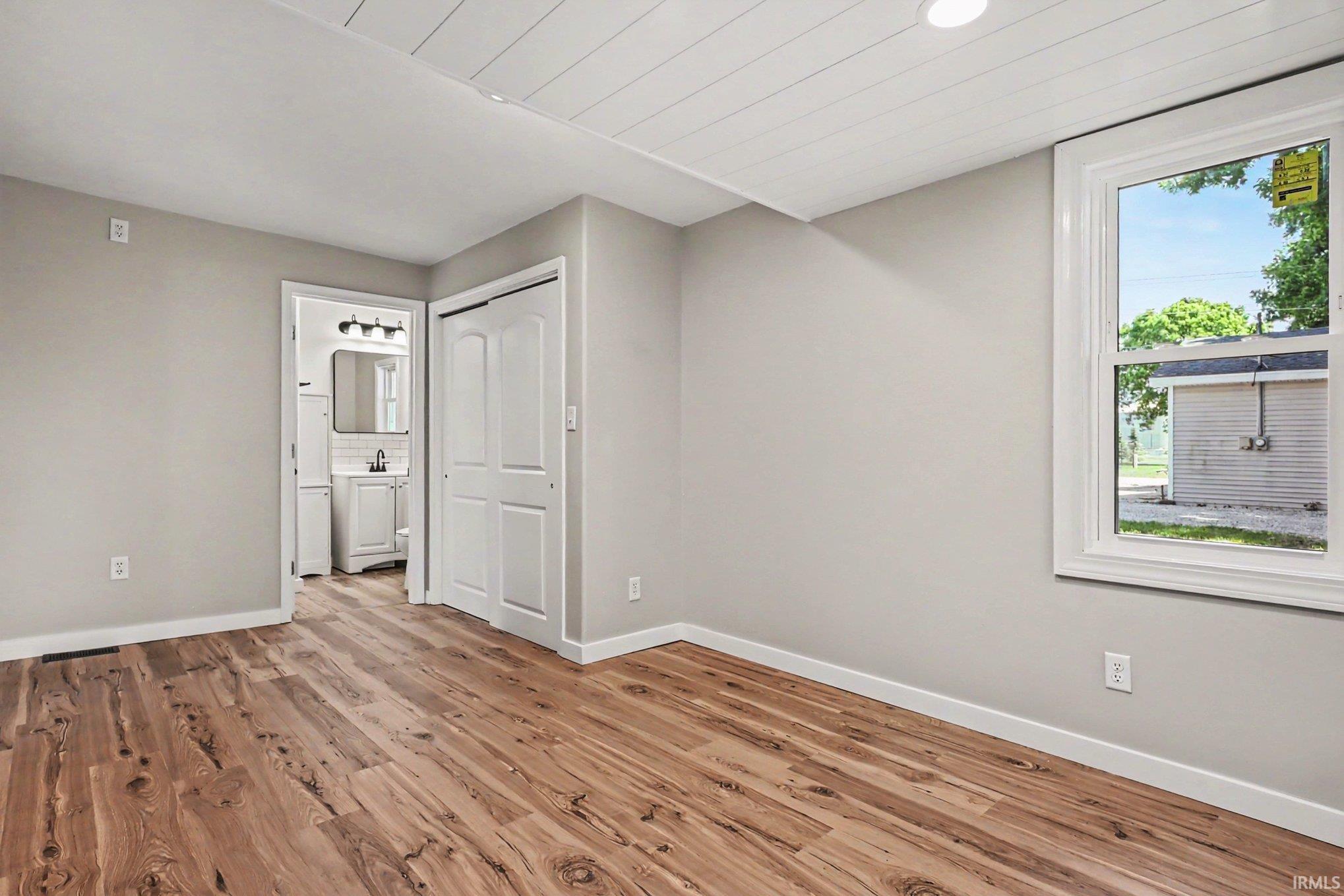 Spacious interior with wood-finish flooring, light gray wall tones, and a white plank ceiling
