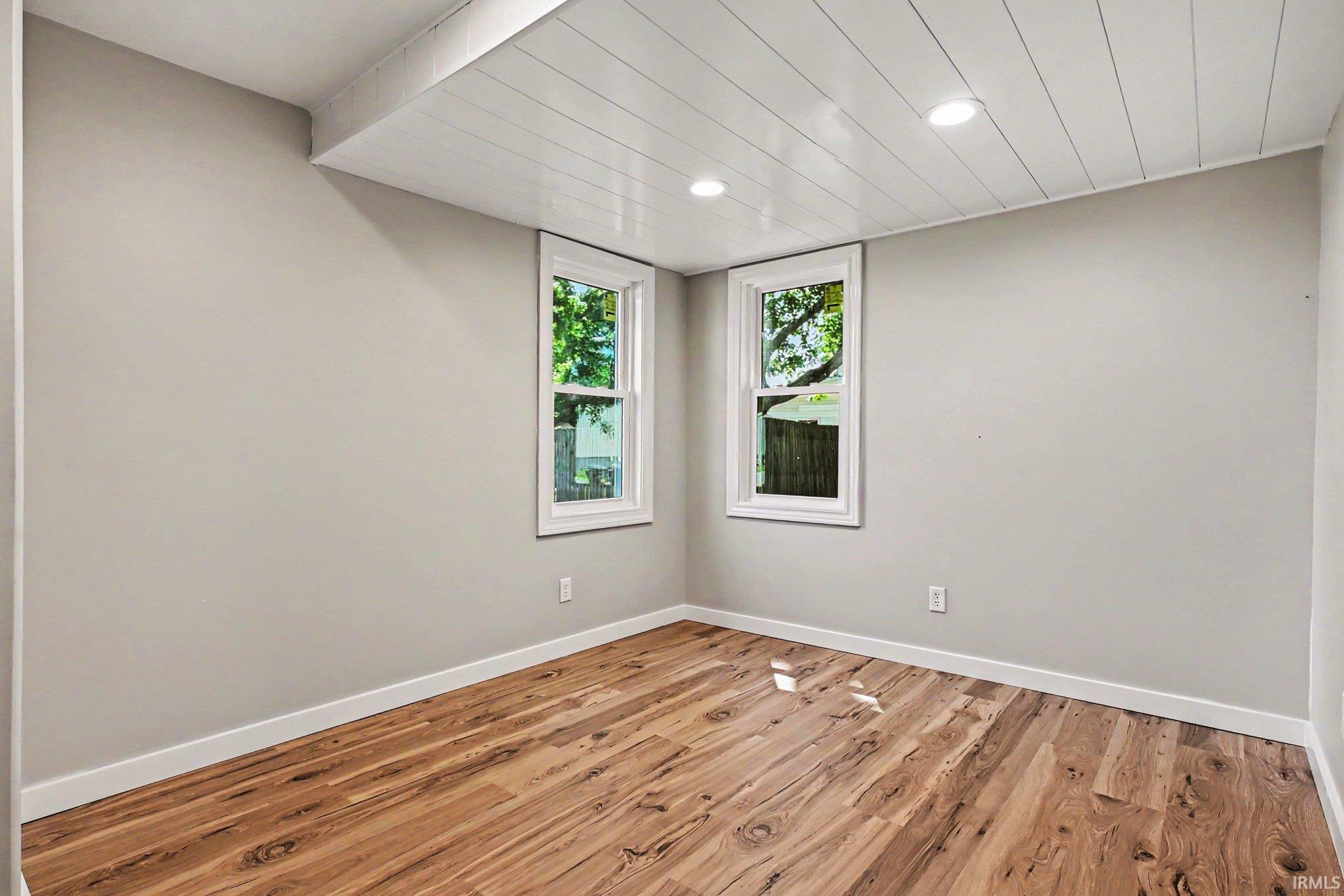 Room with light wood-finish flooring, two white-trimmed windows, a shiplap ceiling with recessed lighting, and neutral wall paint