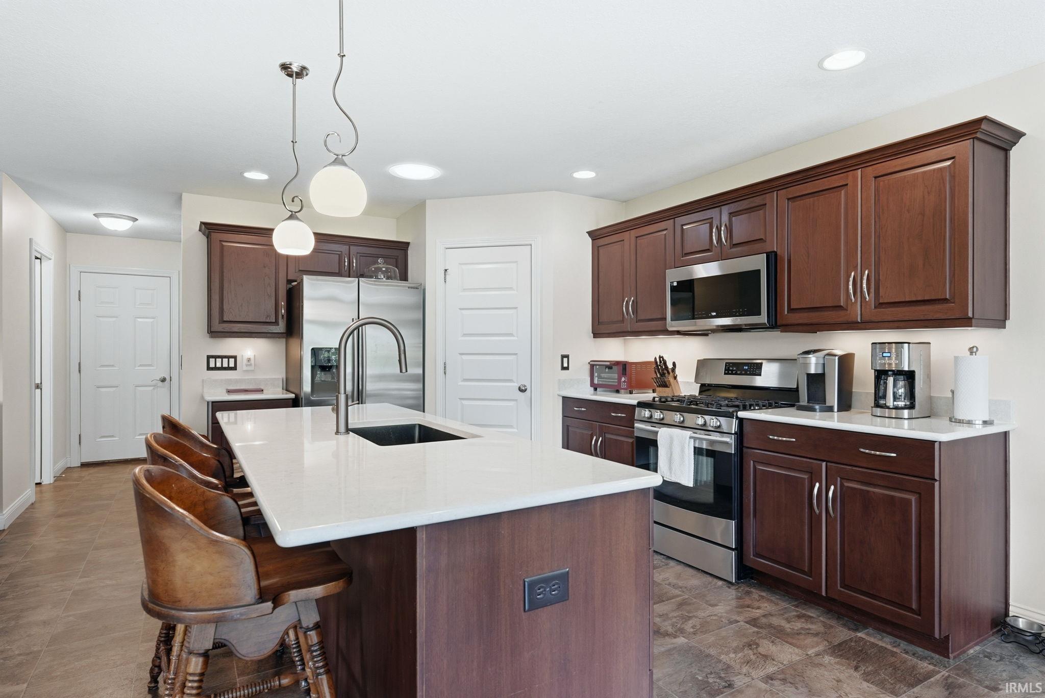 Kitchen featuring a central island with a sink and pendant lighting, rich wood-finish cabinetry, stainless steel appliances, and light-toned countertops