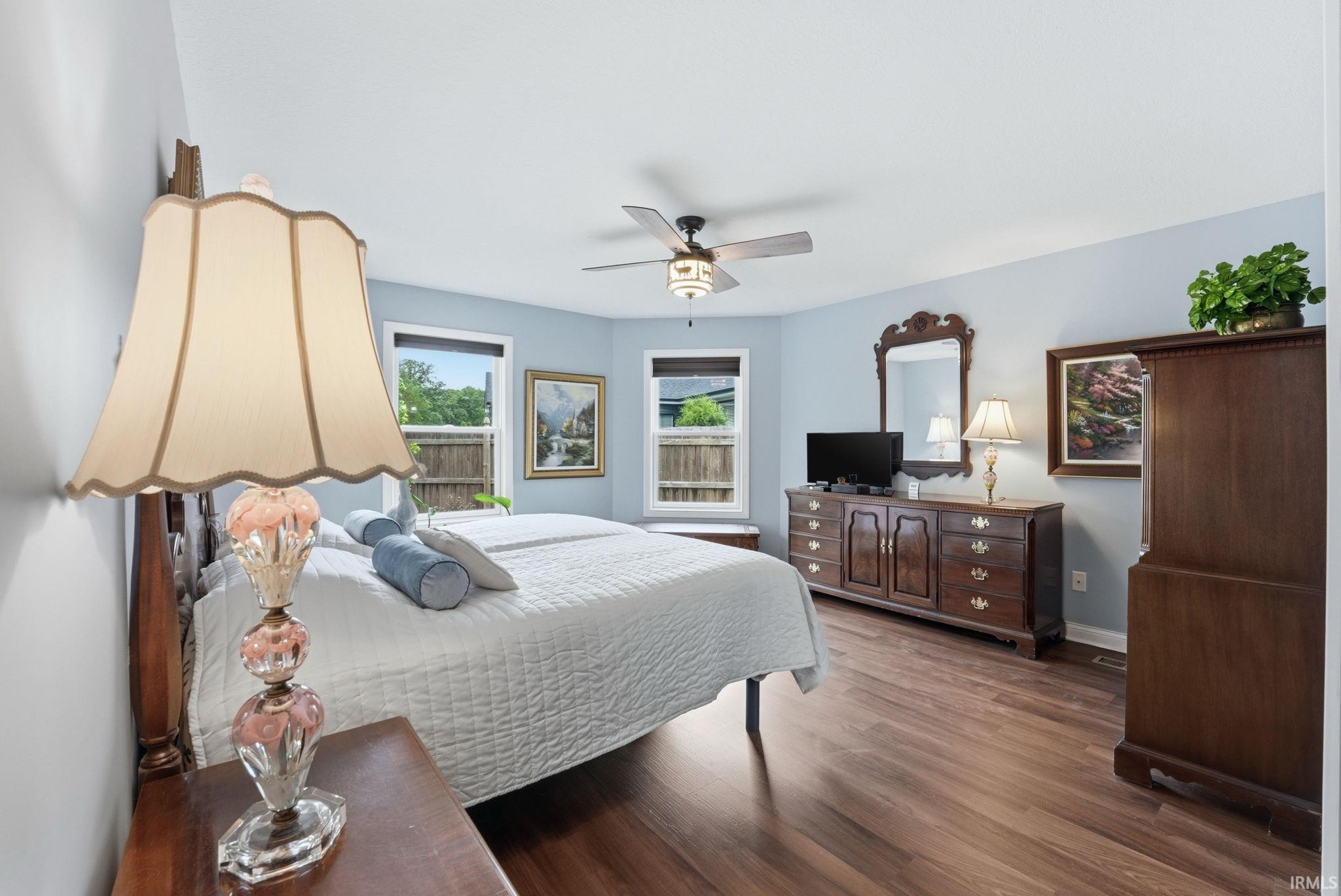 Spacious room featuring wood-finish flooring, light blue wall paint, multiple windows, and a ceiling fan with integrated lighting