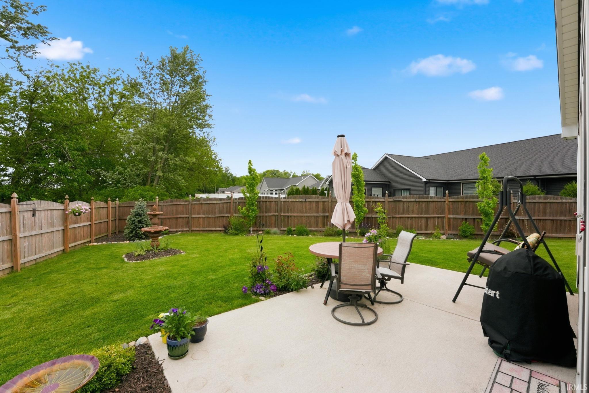 Expansive backyard featuring a concrete patio, a full privacy fence, and a tiered fountain amidst landscaping