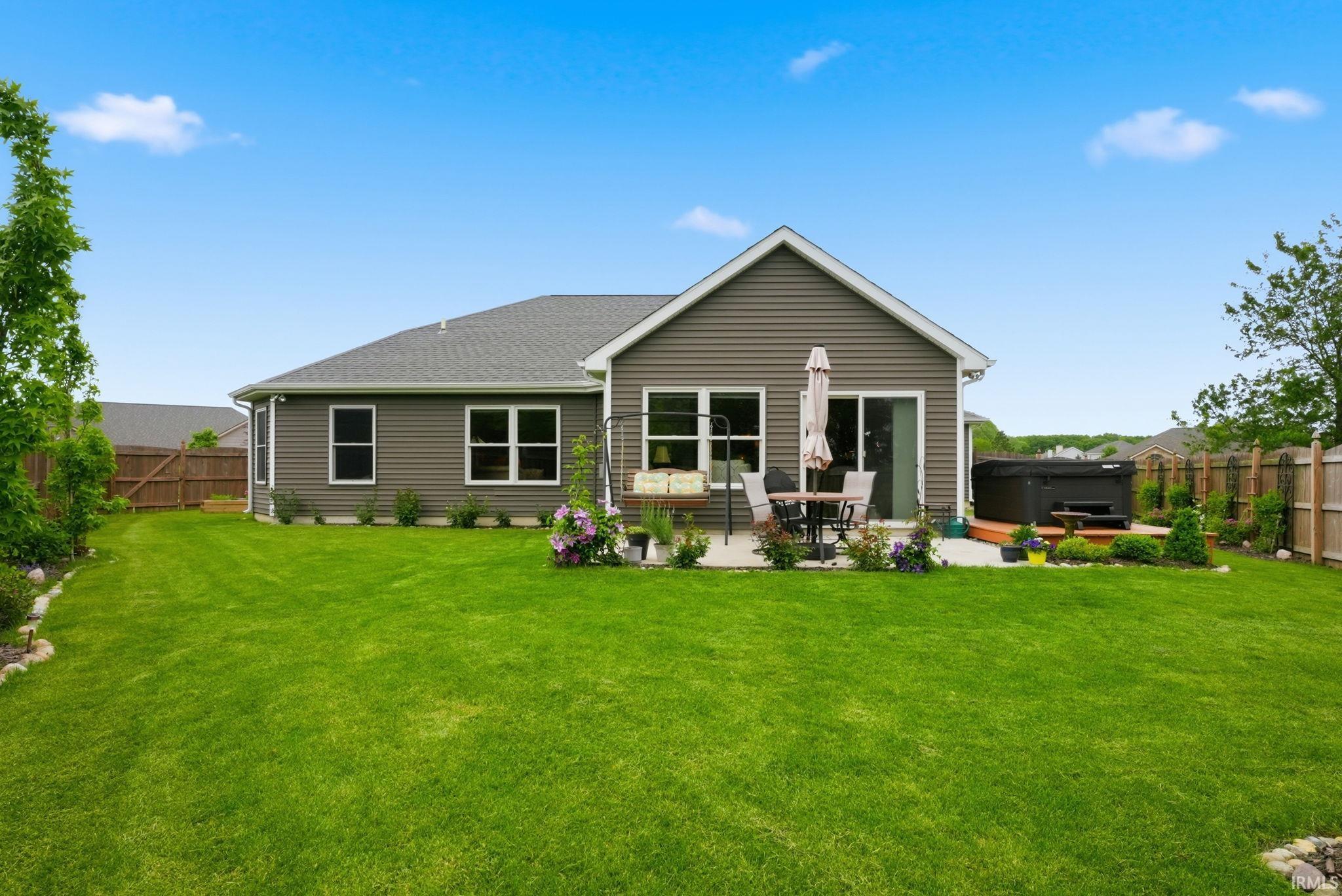 Expansive green lawn surrounds the property, featuring a concrete patio with a built-in hot tub on an elevated wood deck