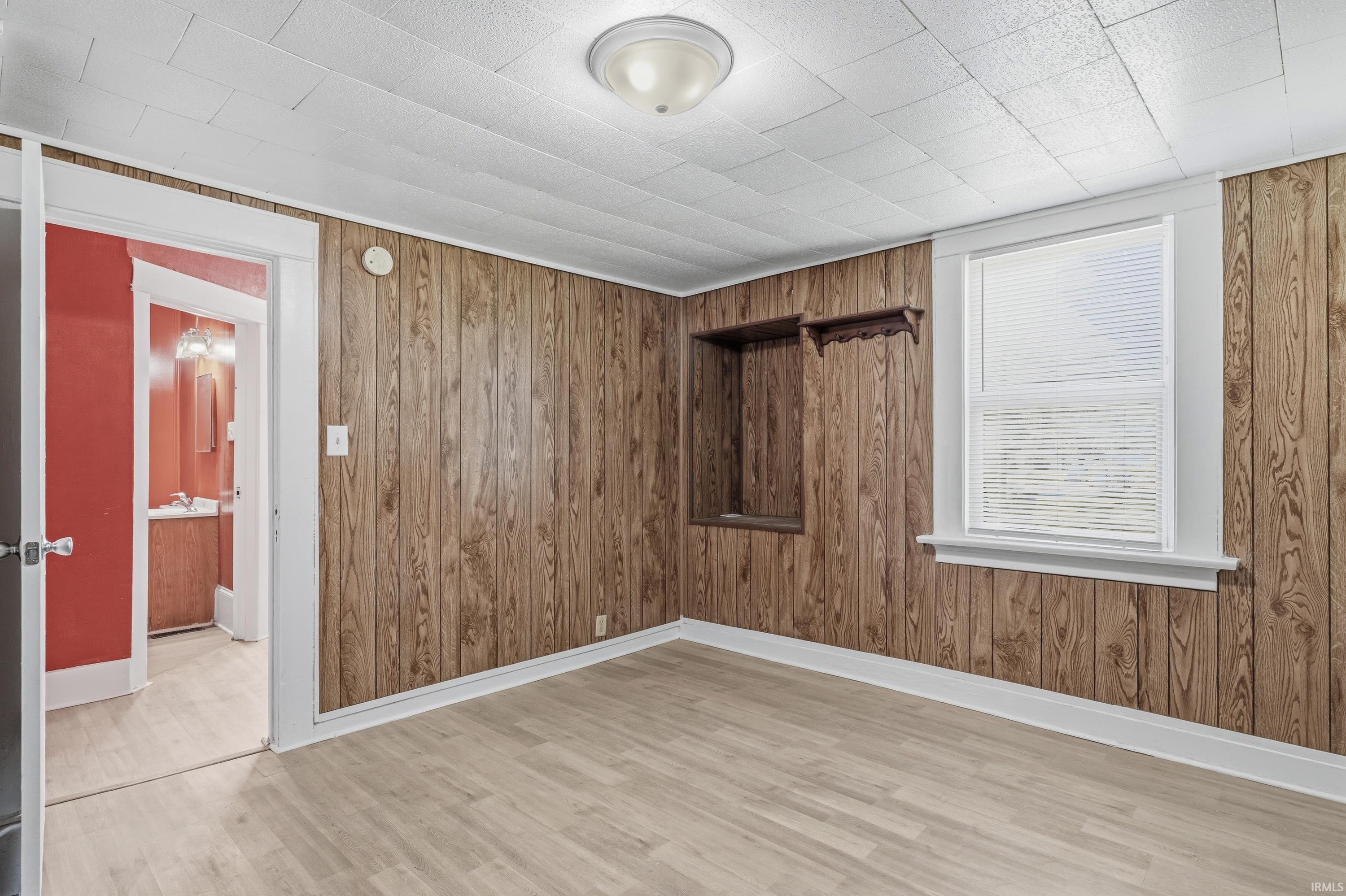 Room featuring wood-finish paneling, light wood-finish flooring, and white trim