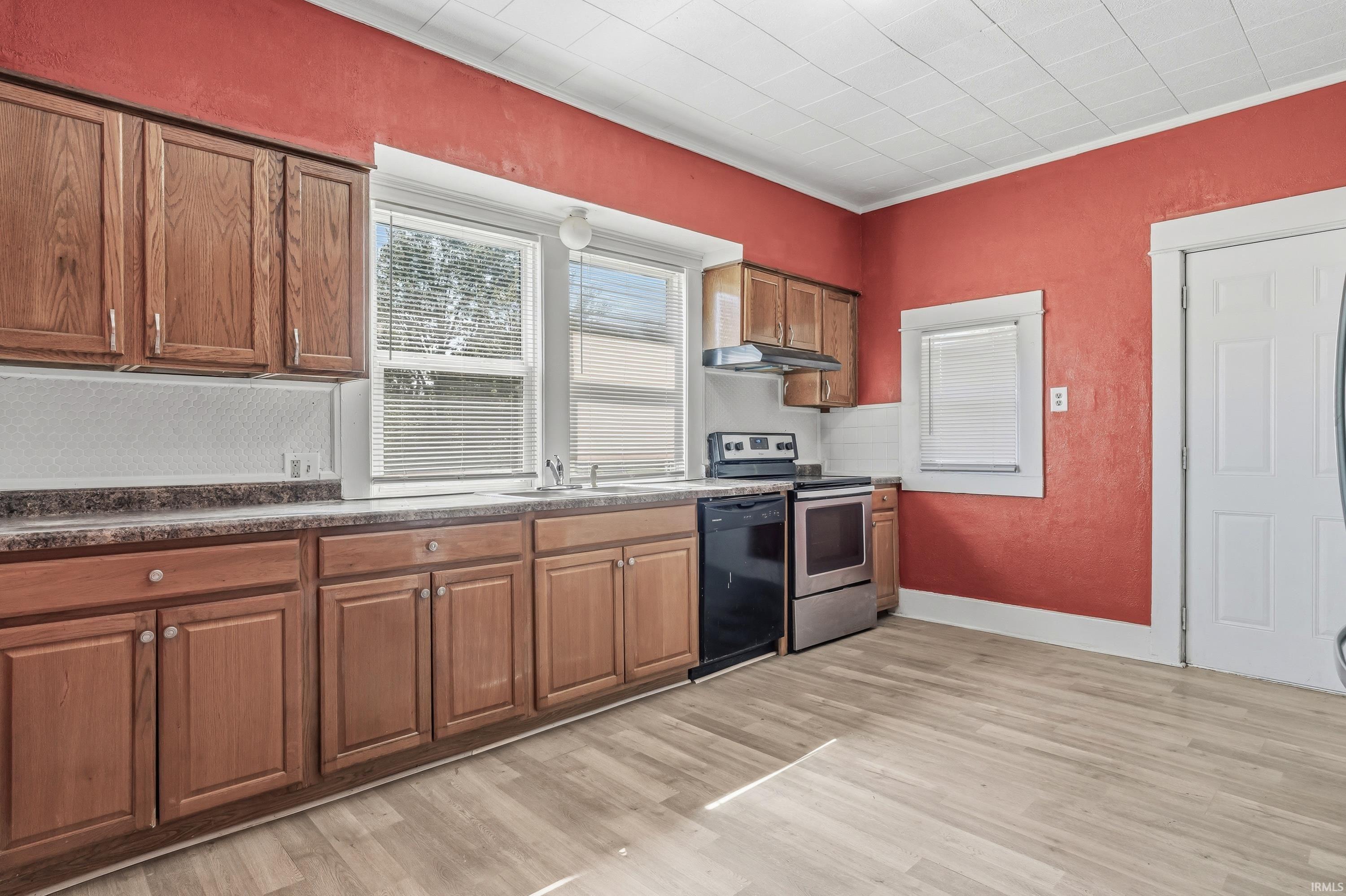 Kitchen featuring light wood-finish flooring, wood cabinetry, a stainless steel and black range, black dishwasher, and a window above the sink