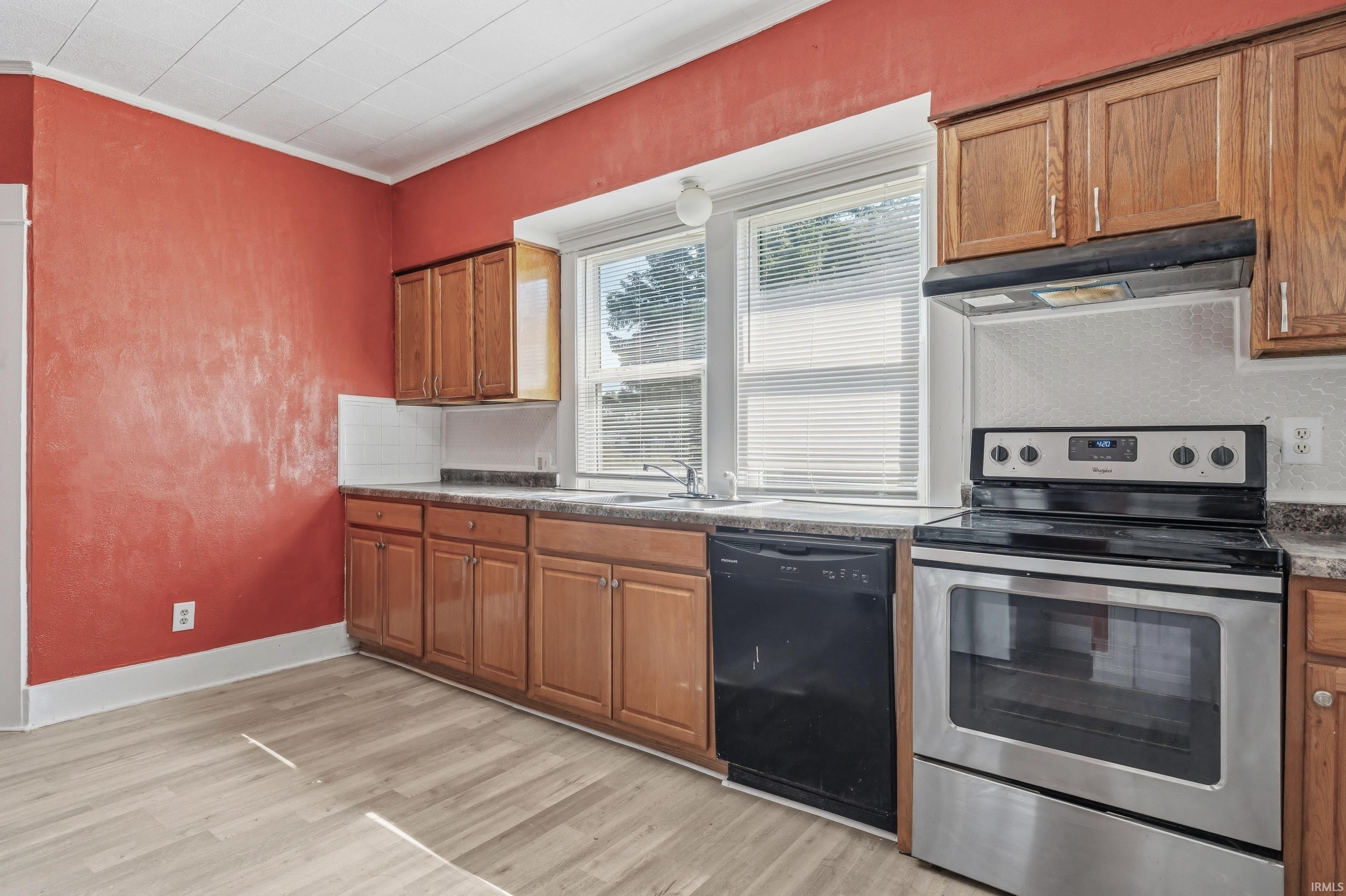 Bright kitchen featuring wood-finish flooring, wood cabinetry, a stainless steel range, and a black dishwasher