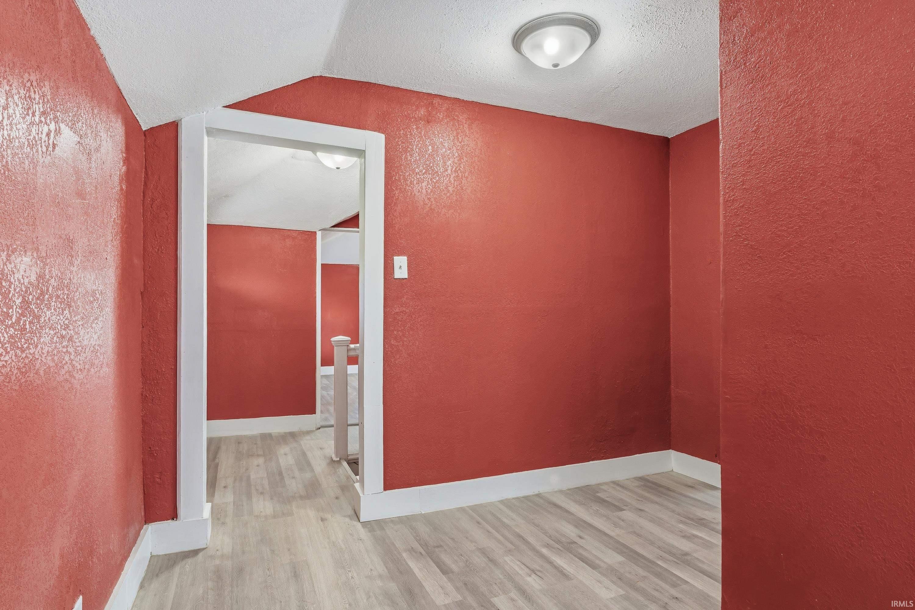 Room with red textured walls, wood-finish flooring, and white trim