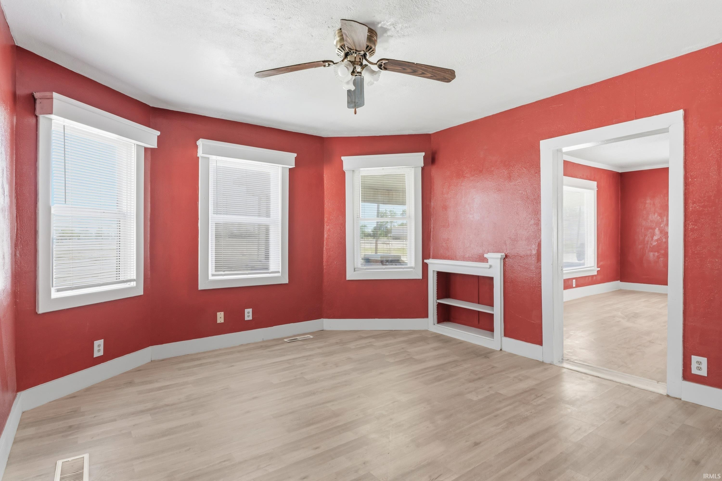 Living area featuring wood-finish flooring, a ceiling fan, multiple windows with white blinds, and a built-in shelving unit