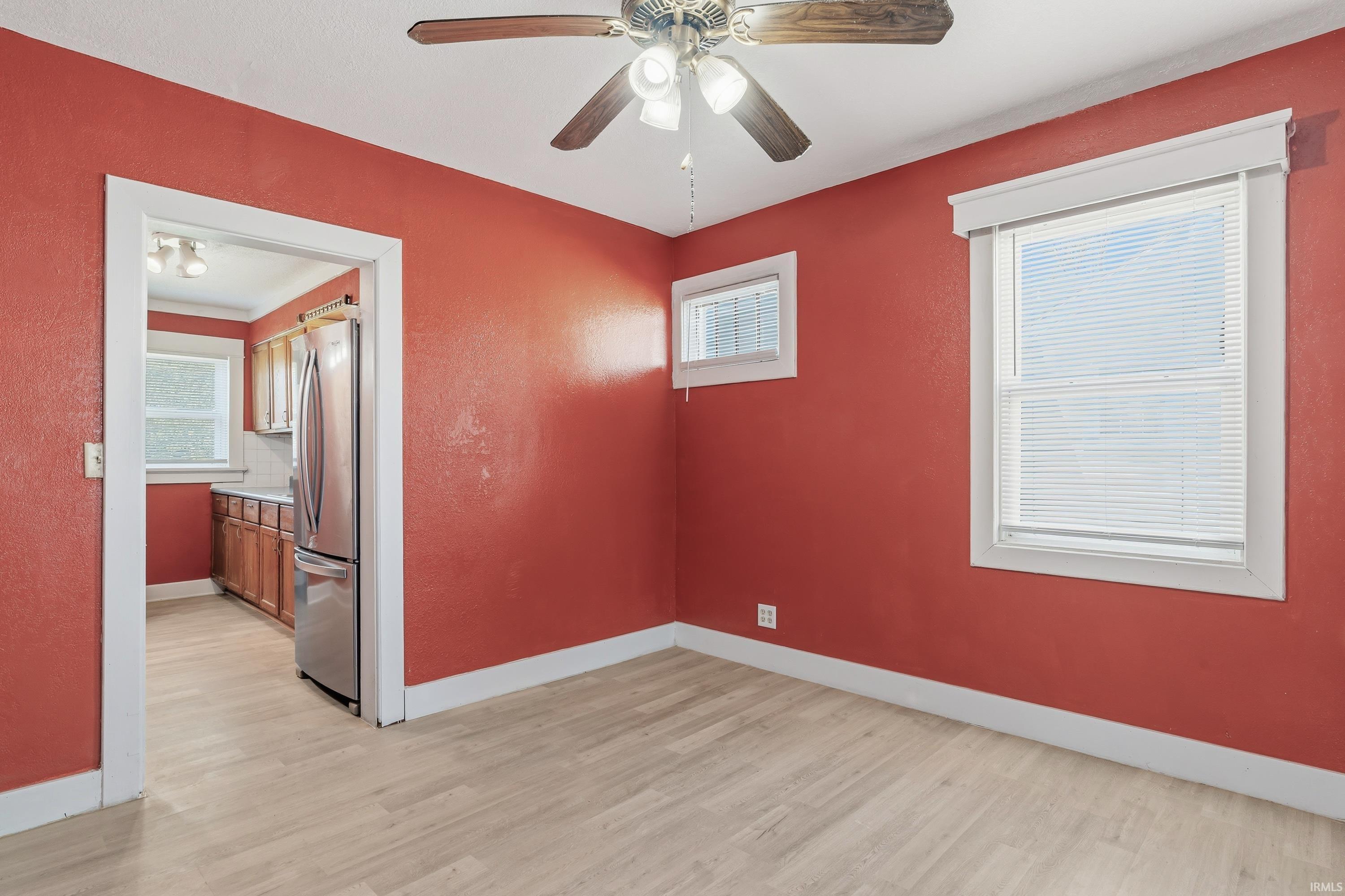 Room featuring wood-finish flooring, a ceiling fan, and multiple windows with blinds