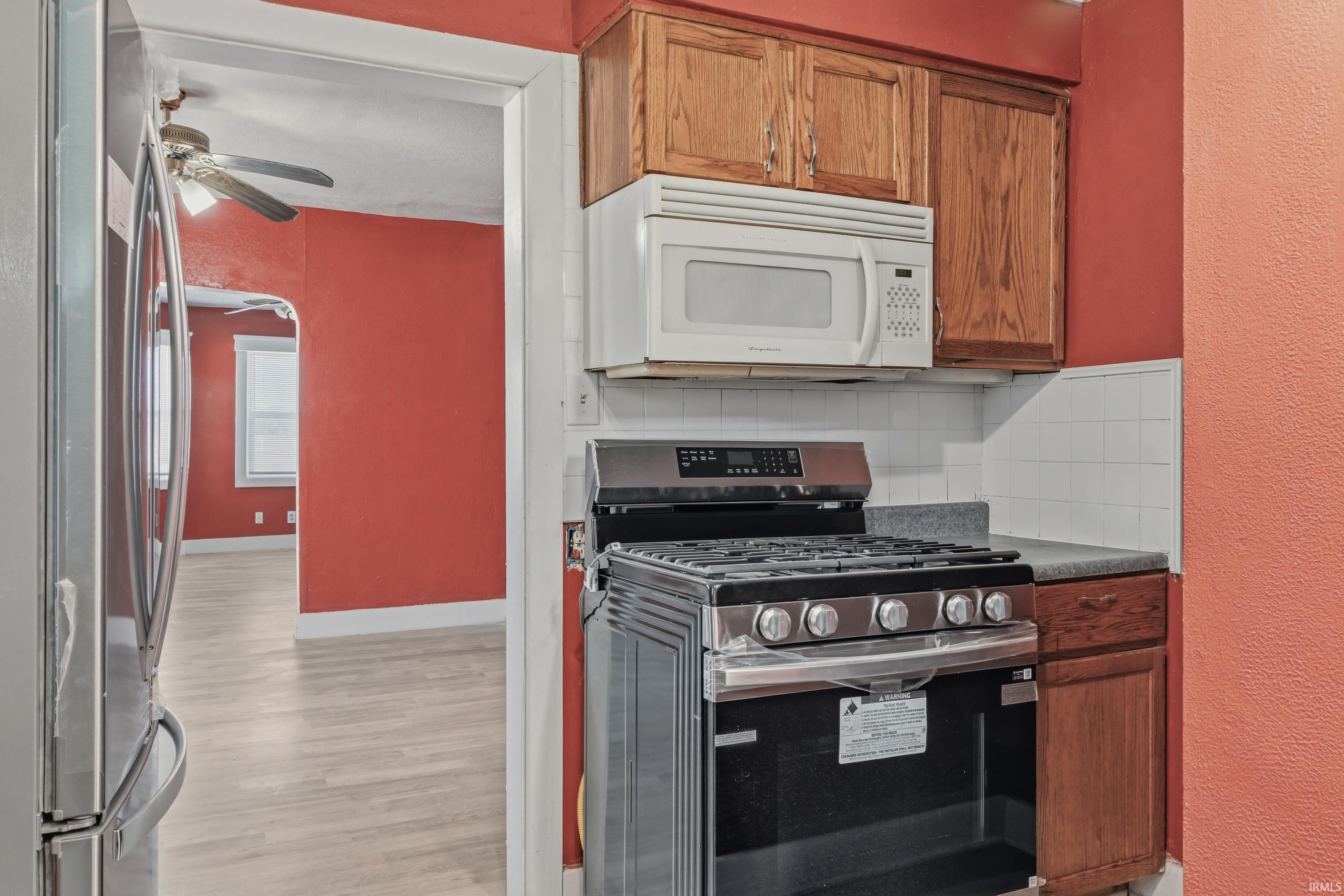 Stainless steel range with an overhead microwave, wood cabinetry, tile backsplash, and light wood-finish flooring
