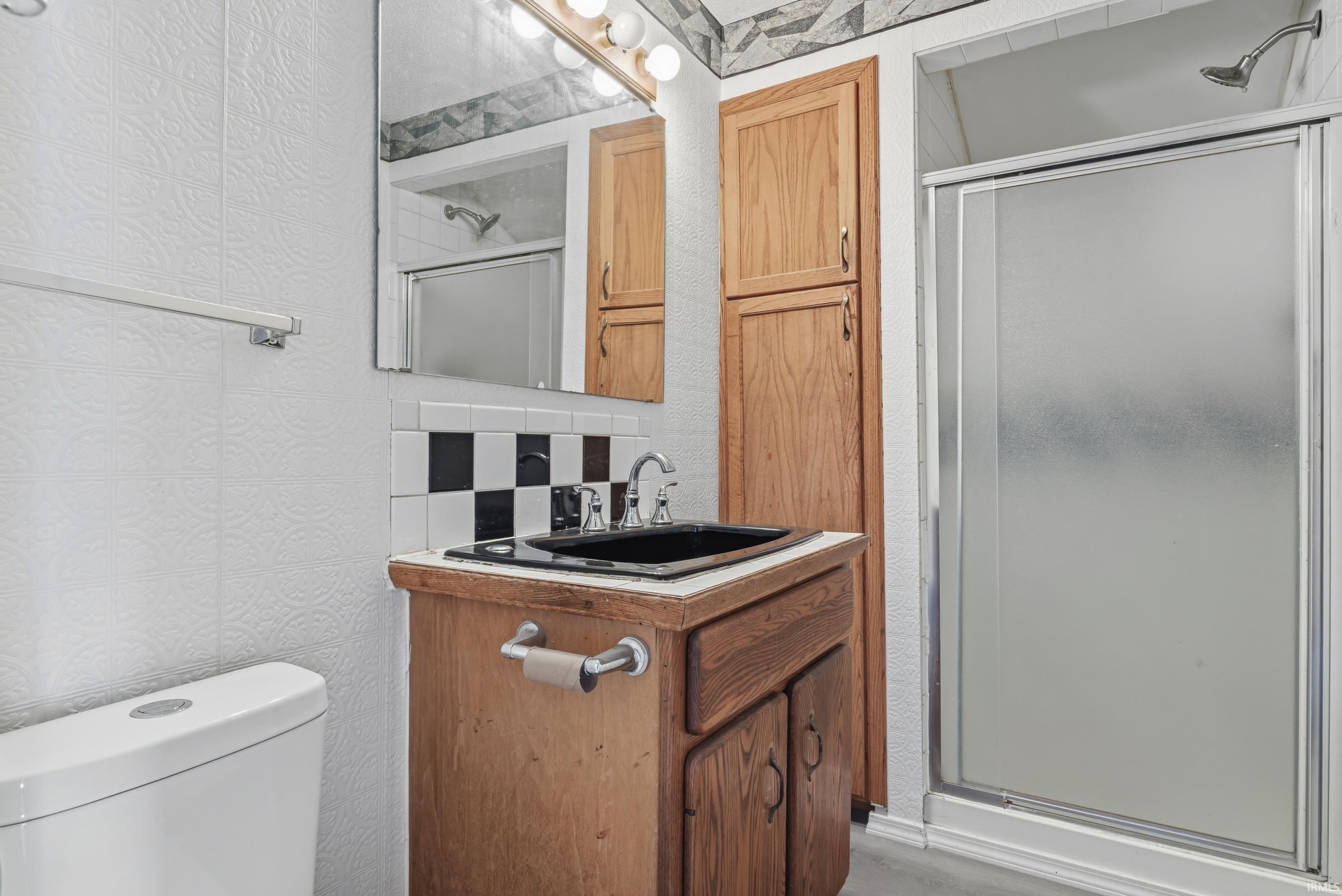 Bathroom featuring a wood vanity with a black basin sink, checkerboard tile backsplash, and a shower with frosted glass doors